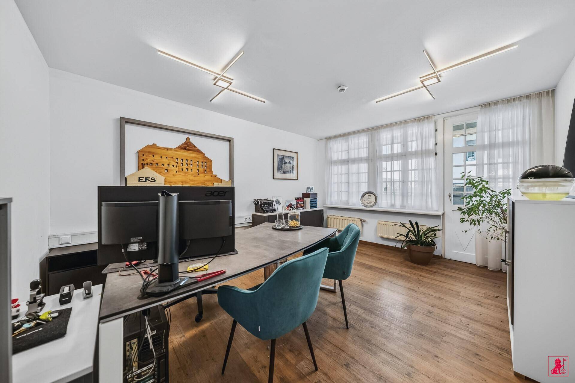 Modernes Büro mit Schreibtisch, ergonomischen Stühlen und großen Fenstern für eine helle Arbeitsatmosphäre.