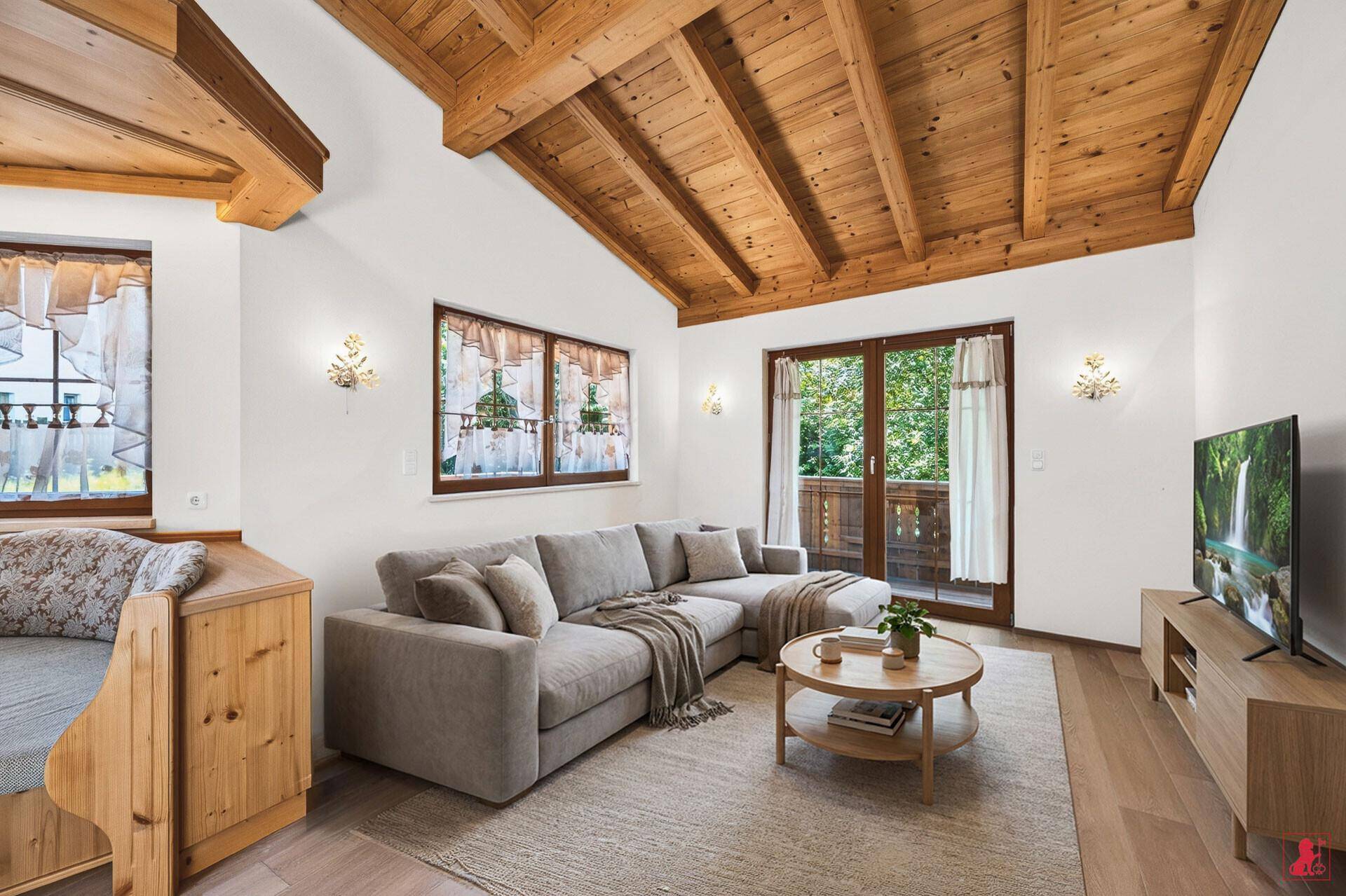 Helles Wohnzimmer mit Sofa, Fernseher, Holzbalkendecke und Balkonzugang.