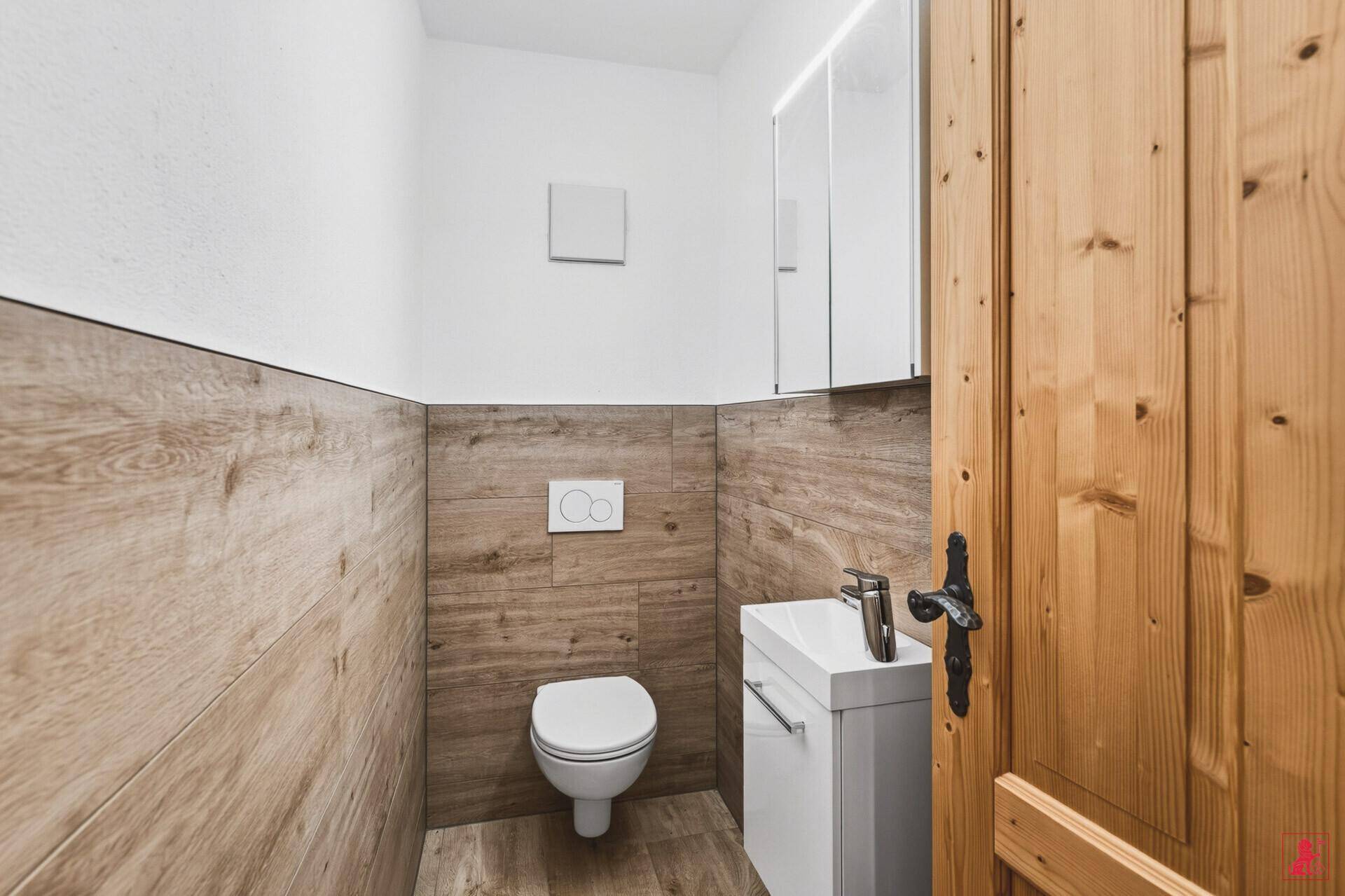 Modernes Gäste-WC mit wandhängender Toilette, kleinem Waschbecken und Holzverkleidung.