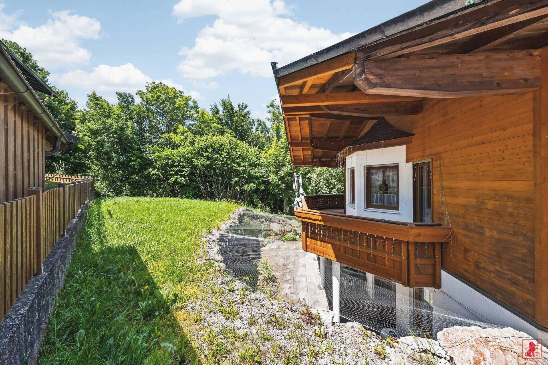 Seitenansicht eines Holzhauses mit traditionellem Balkon, eingebettet in grüne Natur.