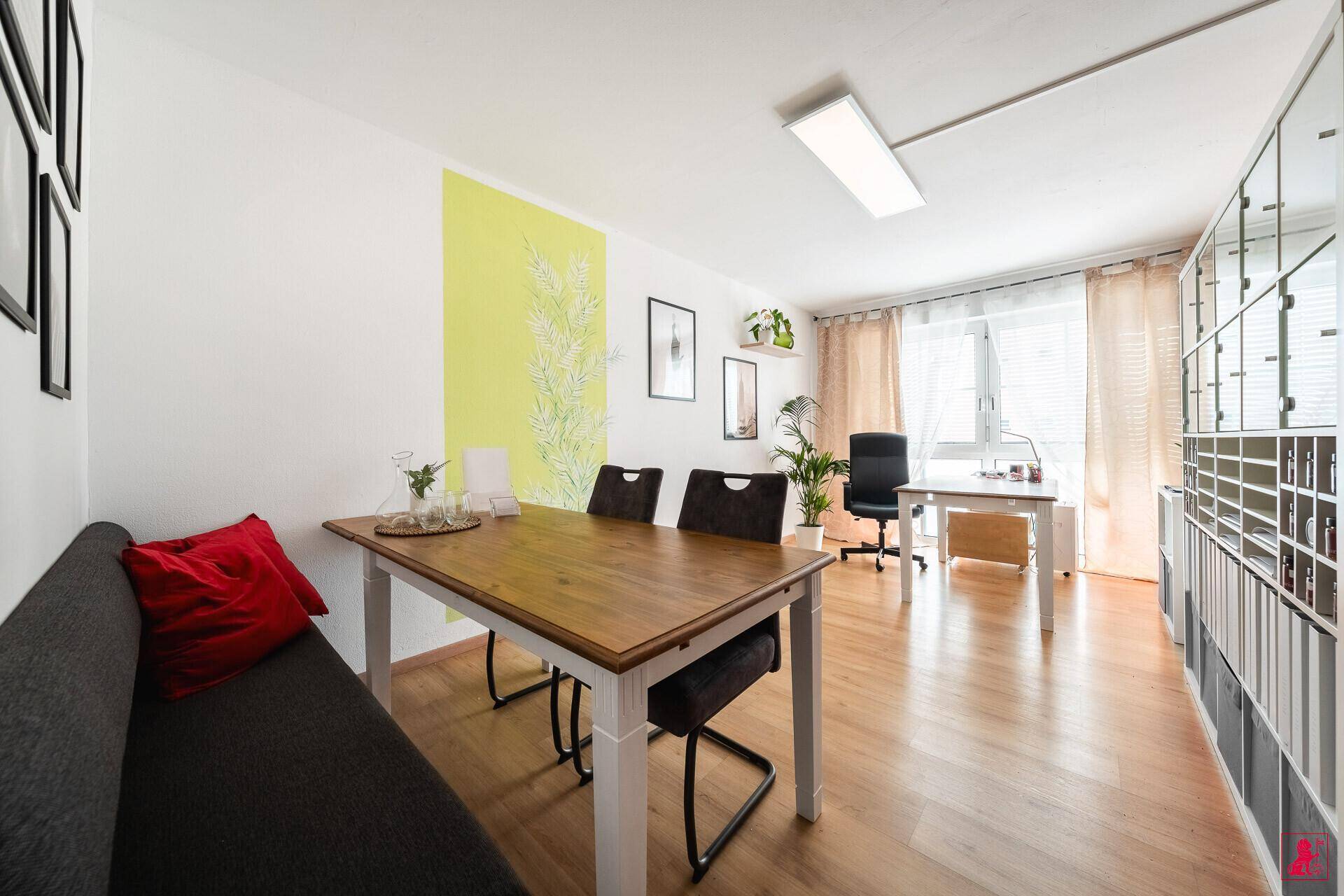 Heller Besprechungsraum mit Holztisch, Sitzbank und Blick auf einen weiteren Arbeitsbereich.