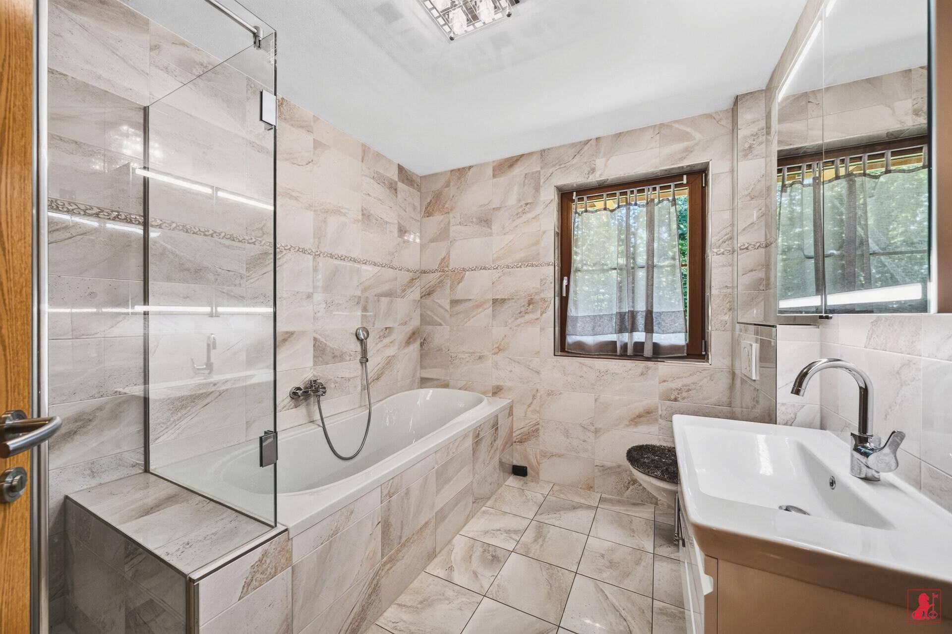 Modernes Badezimmer mit hellen Fliesen, Badewanne mit Duschwand, Einzelwaschbecken und Fenster.