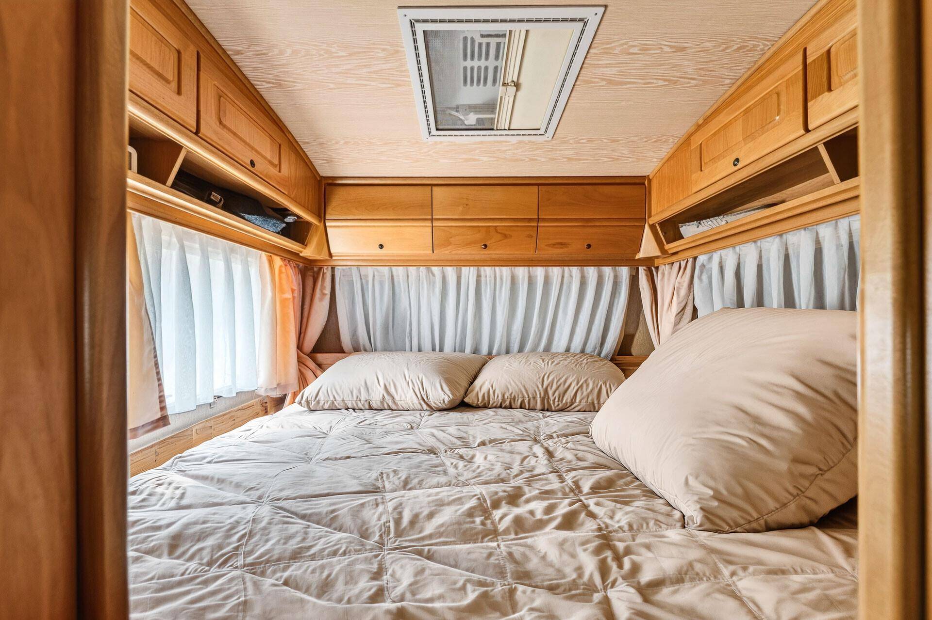 Schlafbereich im Wohnwagen mit Dachfenster und Holzverkleidung, bietet viel natürliches Licht.