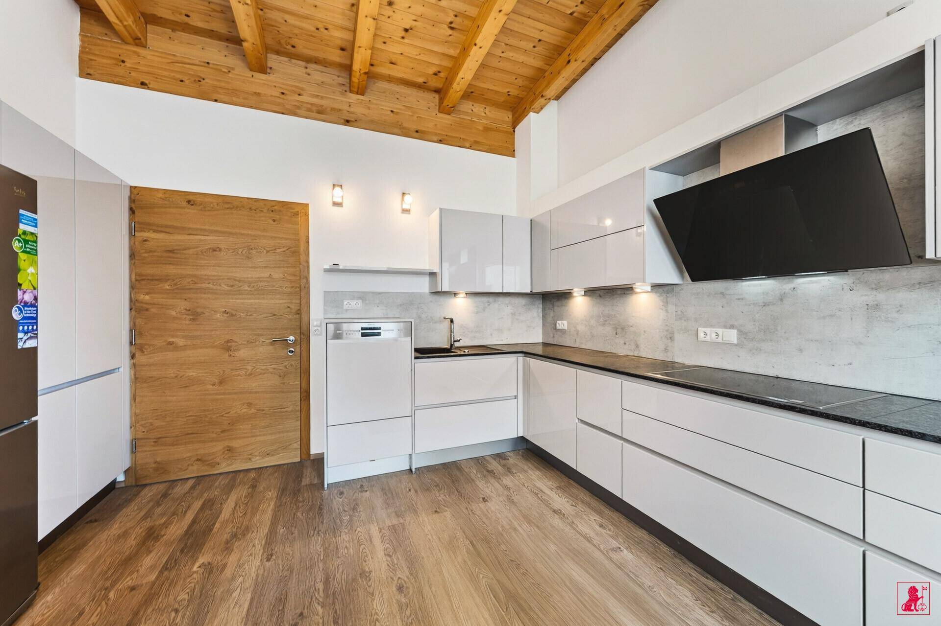 Moderne Küche mit grauen Hochglanzfronten, Holzbalkendecke und integrierten Geräten.