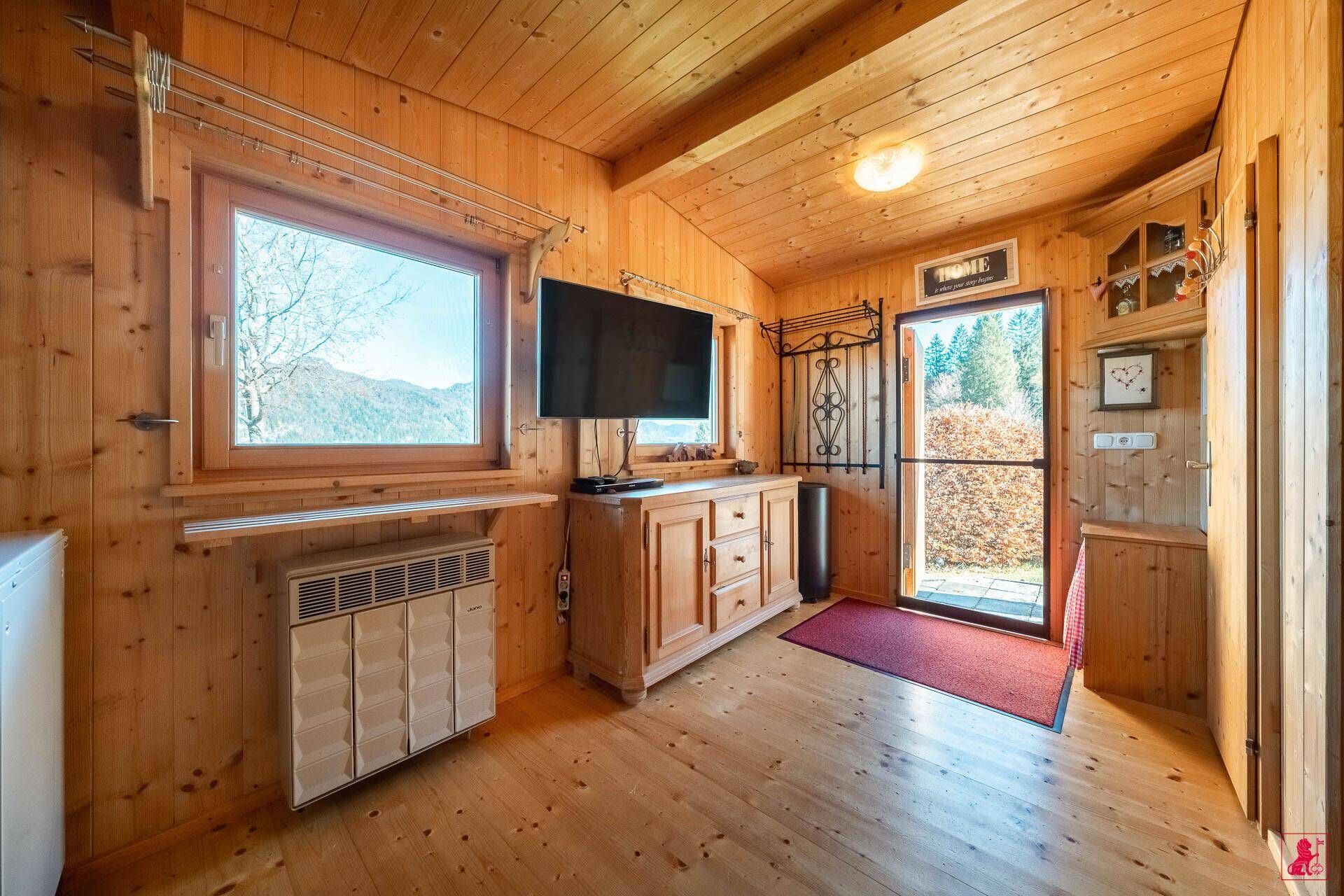Gemütlicher Wohnbereich mit Holzvertäfelung, Fernseher und Blick auf die umliegende Natur.
