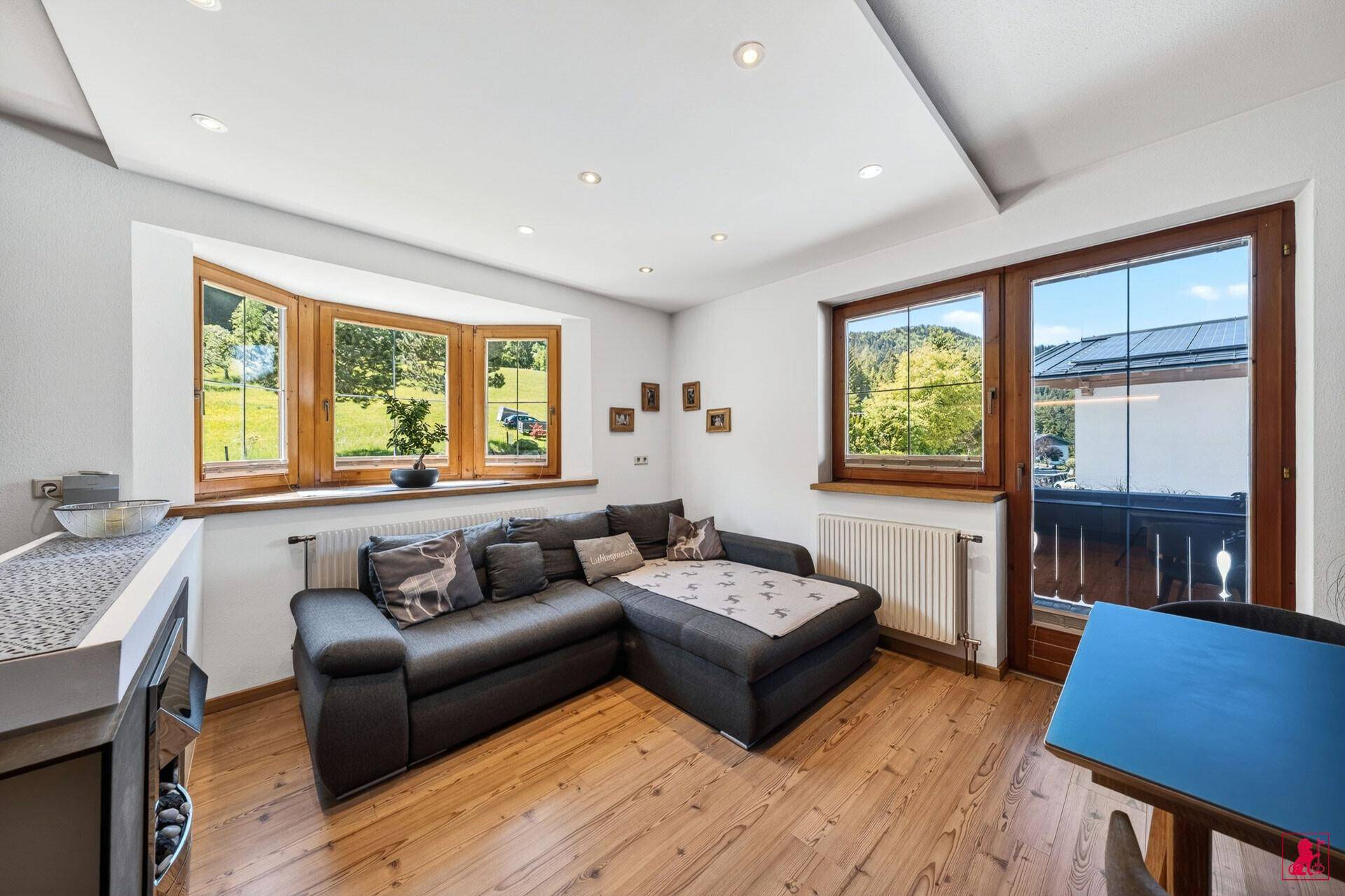Heller Wohnbereich mit Ecksofa, Erkerfenster und Zugang zu einem Balkon.