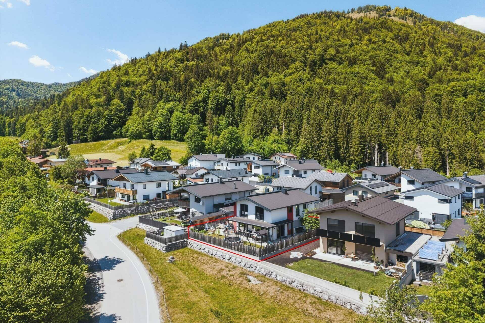 Weitläufige Luftaufnahme eines modernen Einfamilienhauses in einer grünen Wohngegend mit Bergblick.