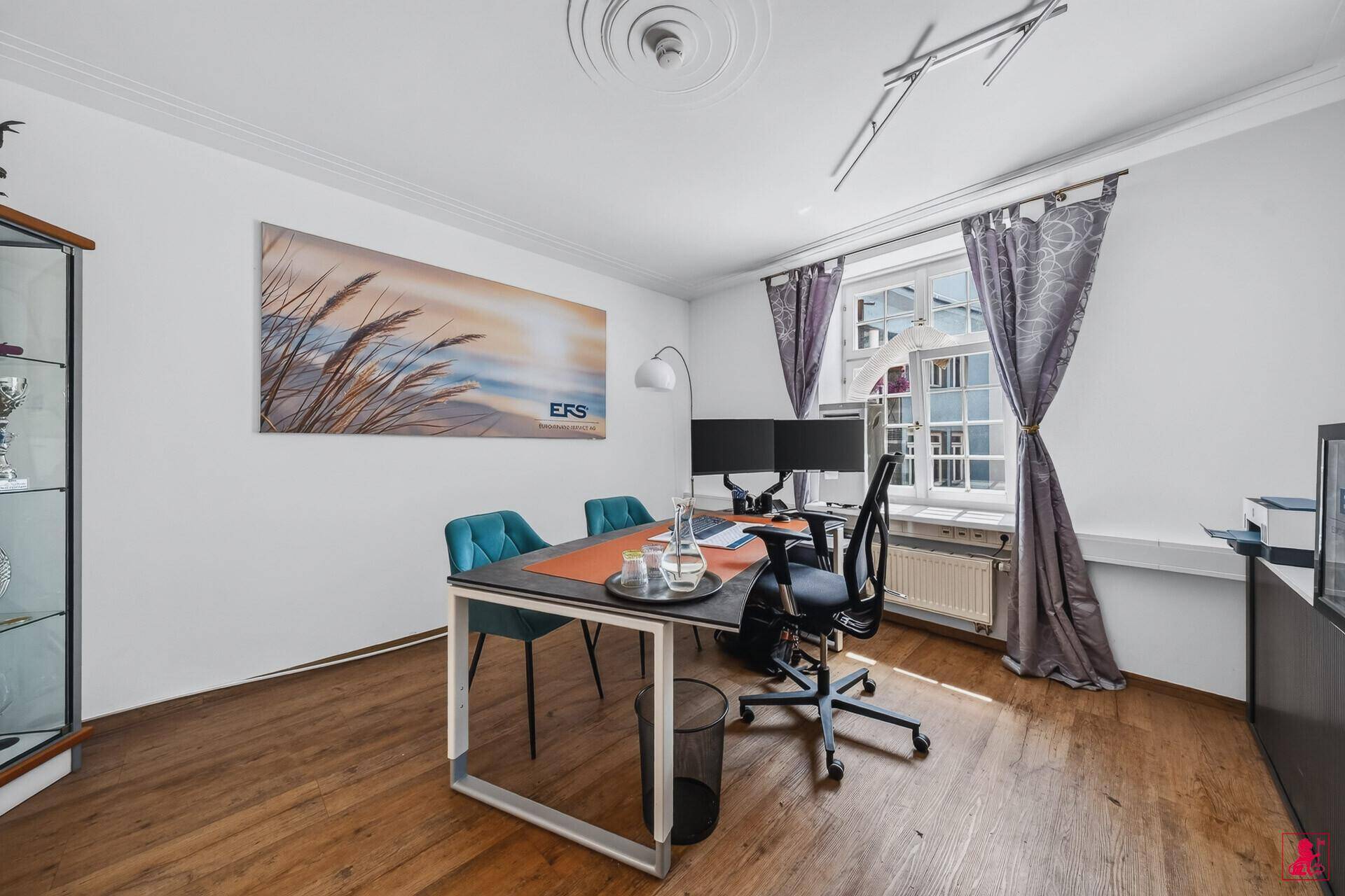 Funktionales Büro mit Schreibtisch, Bürostuhl und einem Fenster mit Vorhängen, das den Raum erhellt.