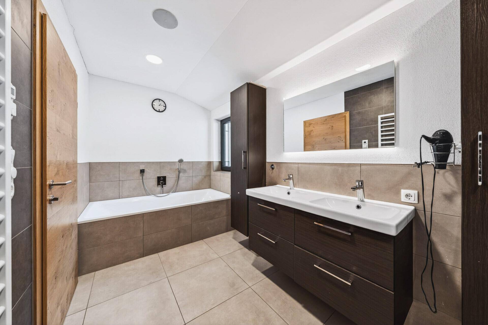 Modernes Badezimmer mit Badewanne, Doppelwaschbecken und großem Spiegel, gut beleuchtet.
