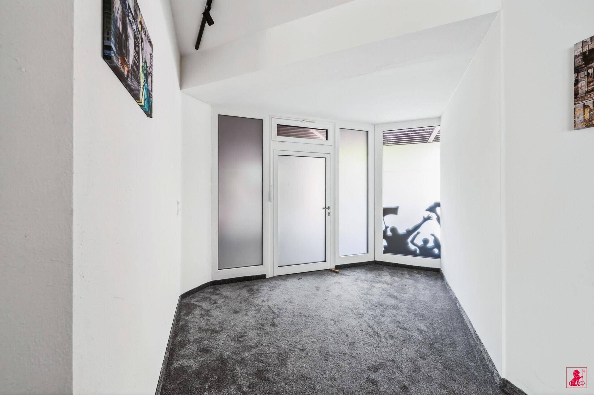 Eingangsbereich mit grauem Teppichboden, weißen Wänden und einer modernen Glastür mit Seitenfenstern.