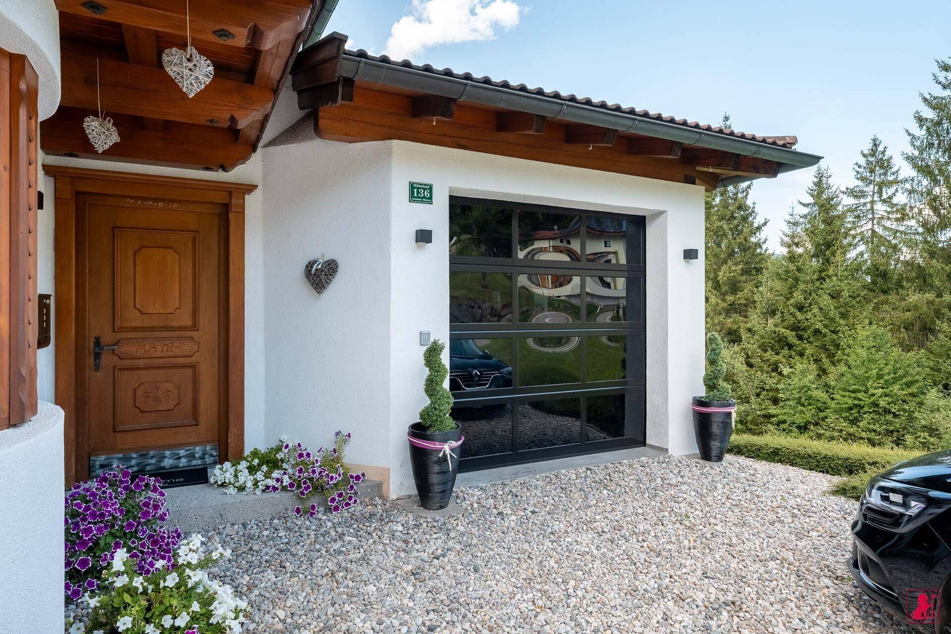 Eingangsbereich des Hauses mit Holztür, Garage und gepflegter Bepflanzung.