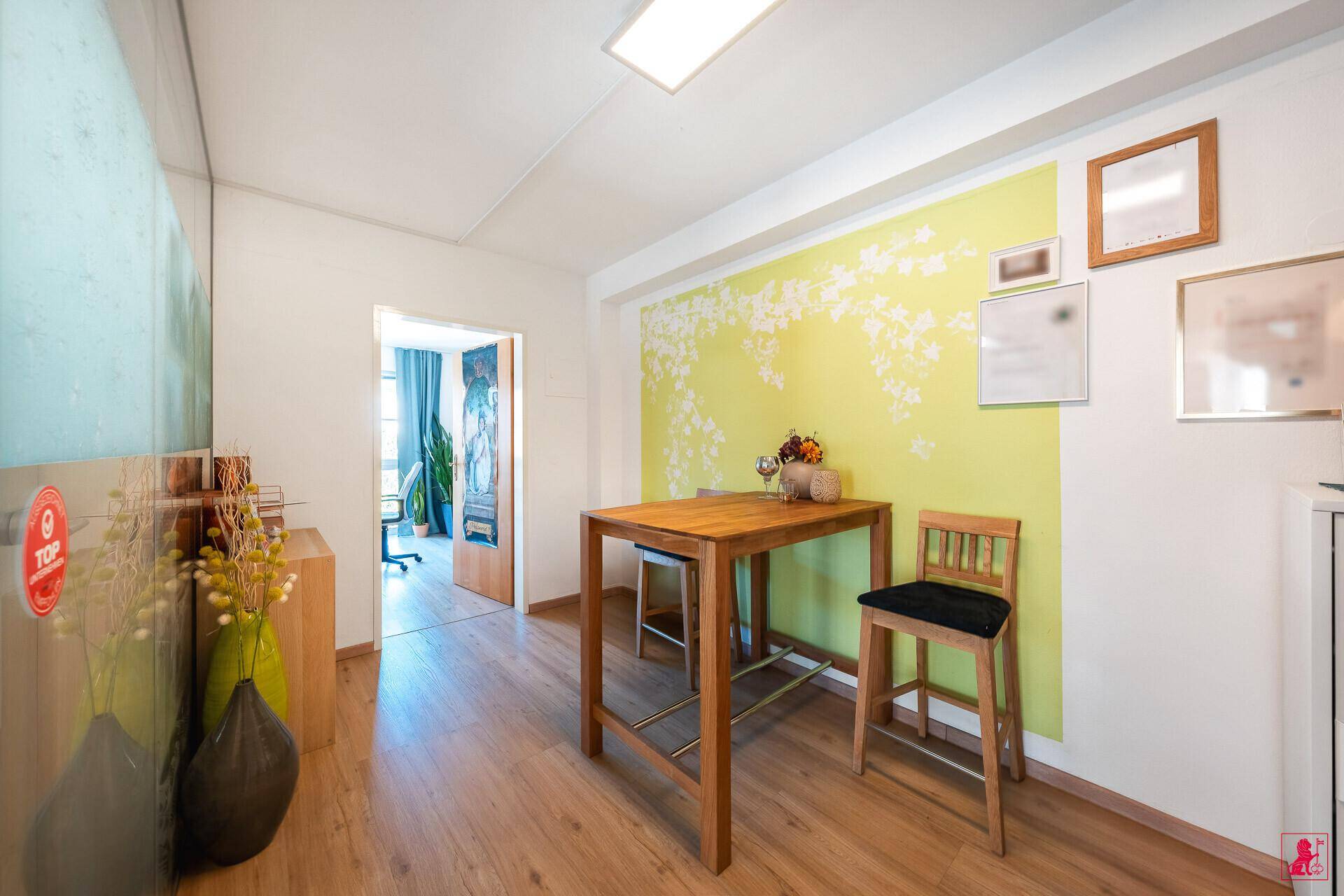 Gemütlicher Barbereich mit Holztisch und Hockern, angrenzend an einen weiteren Arbeitsbereich.