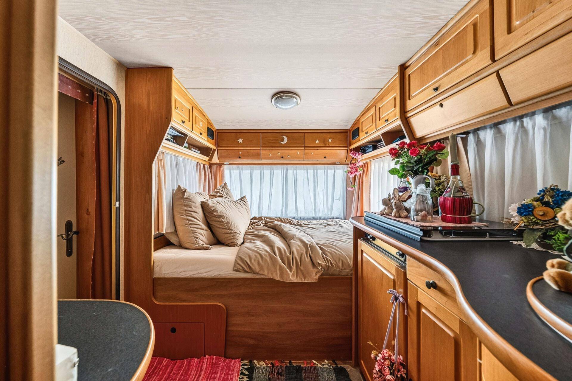Gemütliches Schlafzimmer in einem Wohnwagen mit Holzeinbauten und Stauraum über dem Bett.