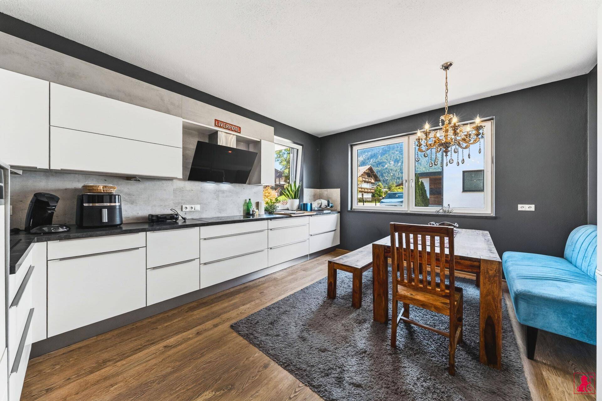 Moderne Wohnküche mit weißen Schränken, Esstisch und Bergblick durch das Fenster.