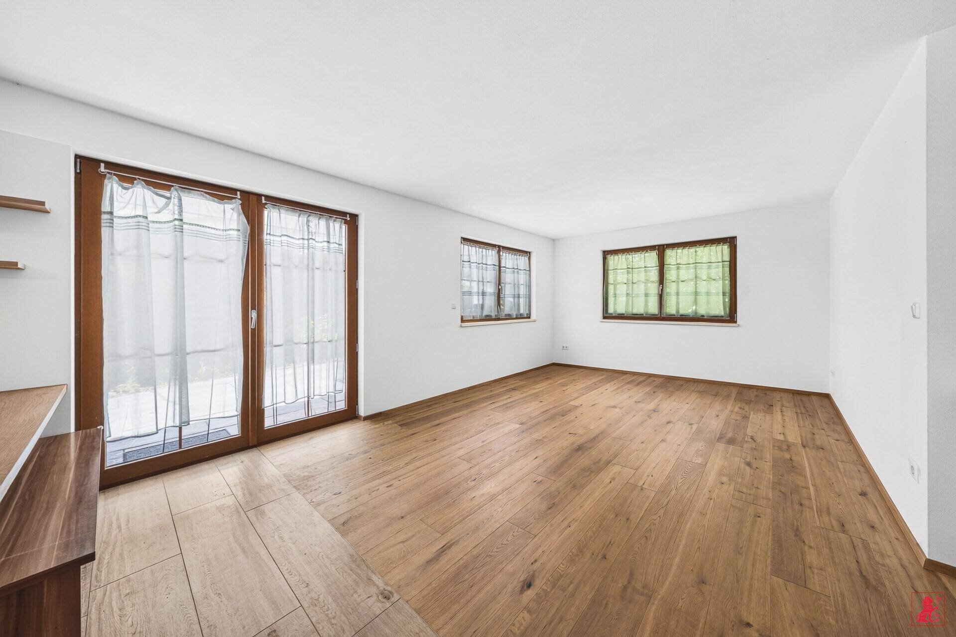 Helles, leeres Wohnzimmer mit Holzboden und großen Fenstern, bereit zur individuellen Gestaltung.