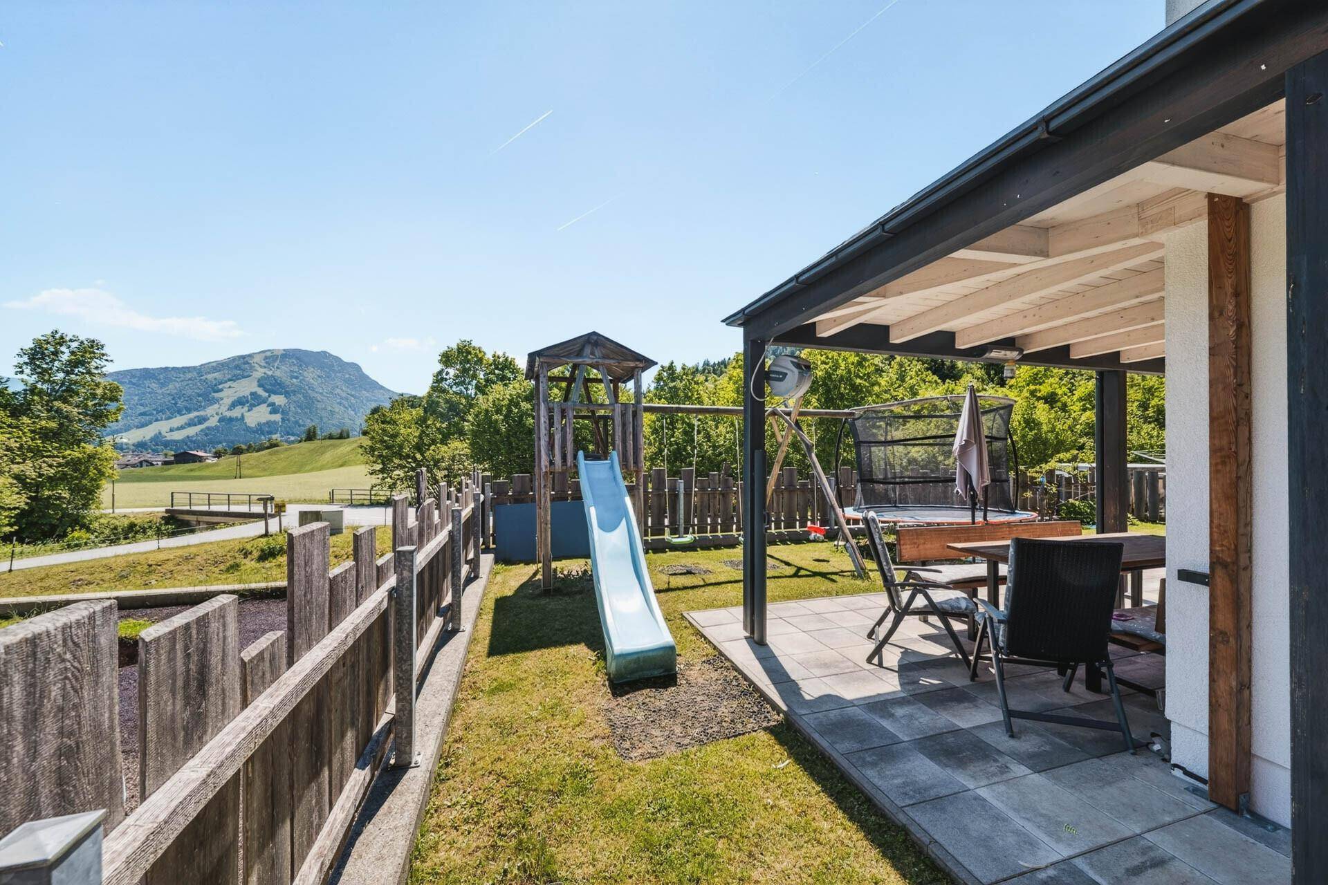 Großer Garten mit Spielplatz, Rutsche und Schaukel, umgeben von einer Holzterrasse.