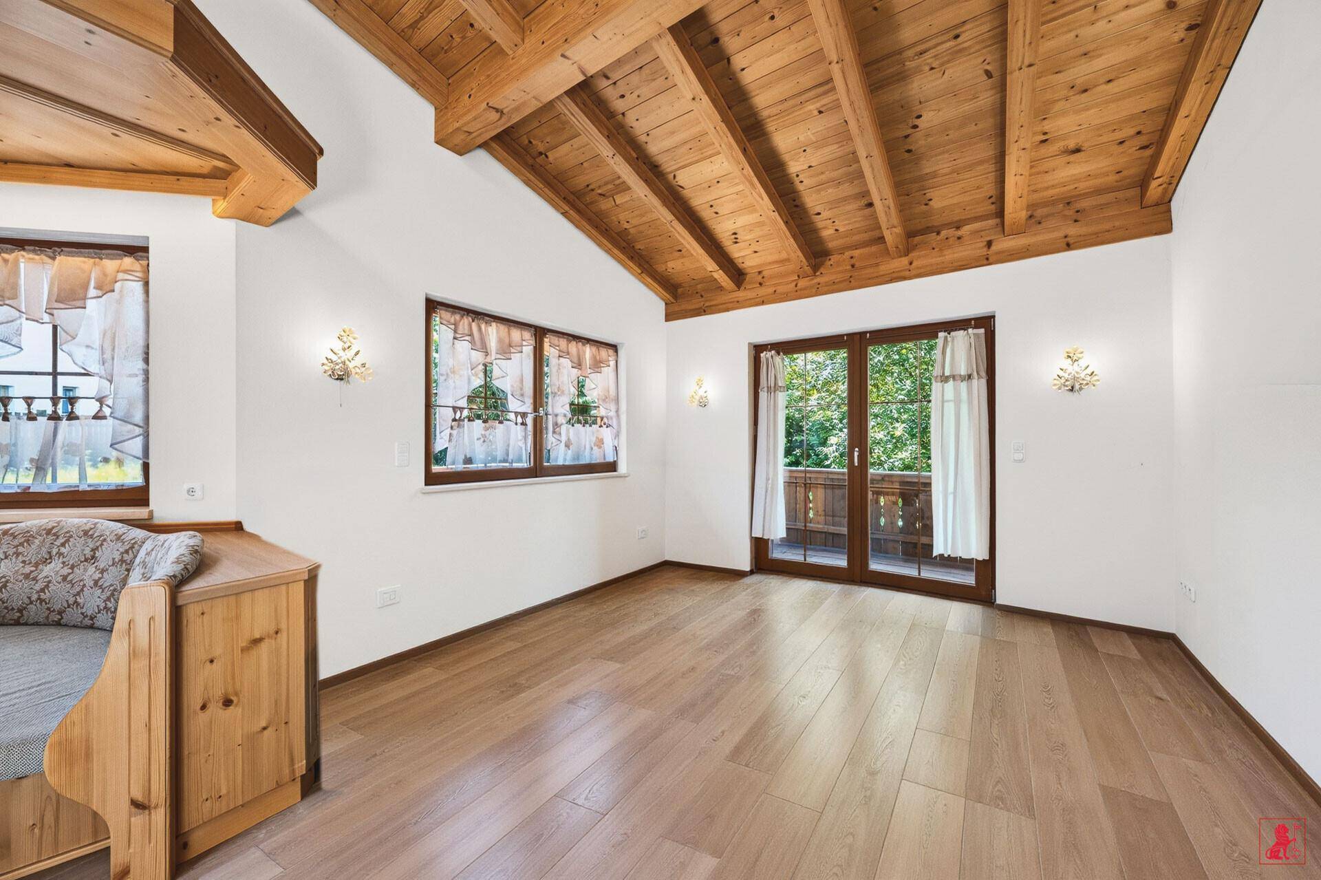 Geräumiges Wohnzimmer mit Holzbalkendecke, Holzboden und Zugang zum Balkon.