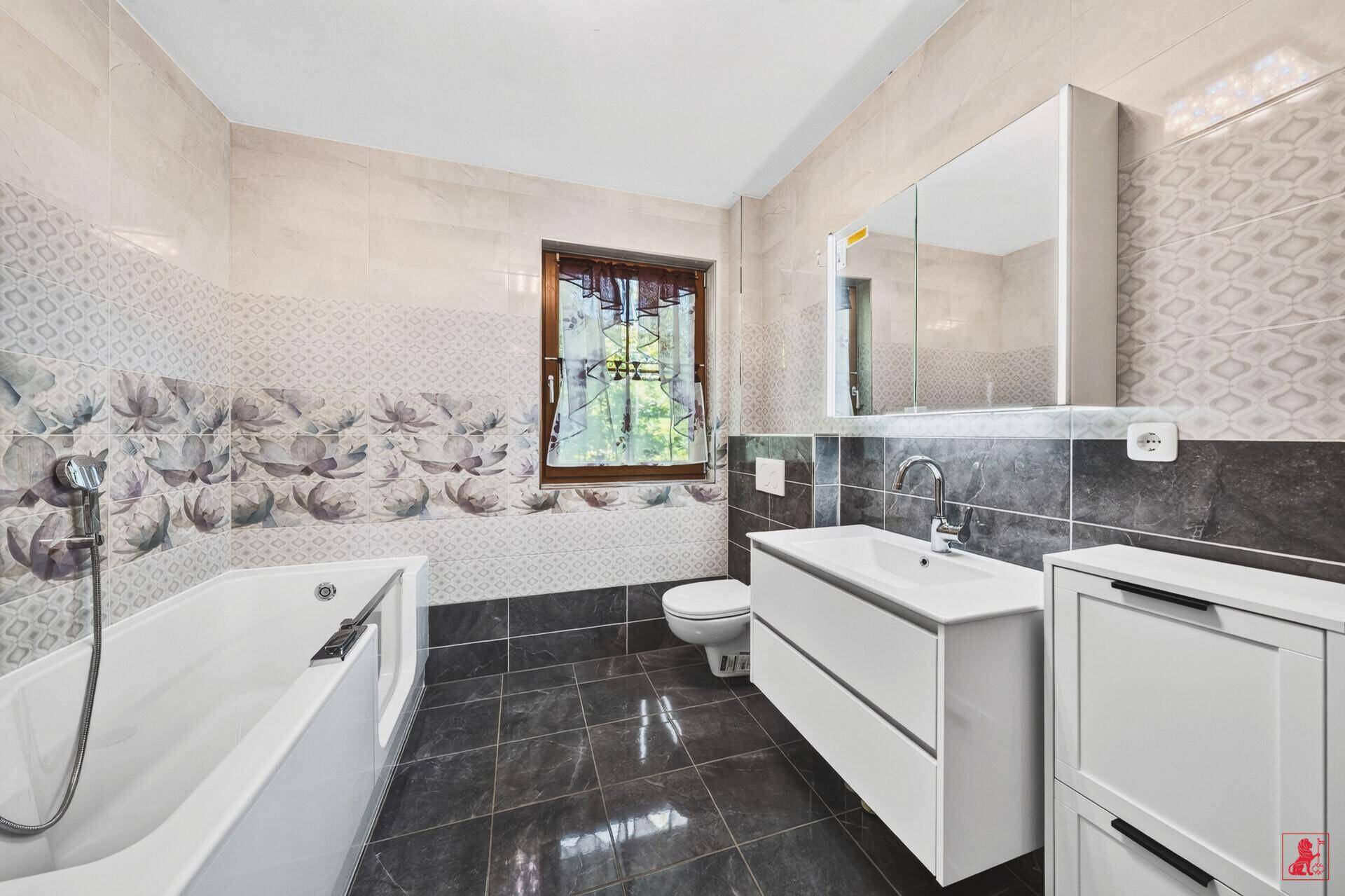 Badezimmer mit modernem Waschtisch, Toilette, Spiegelschrank und Fenster.