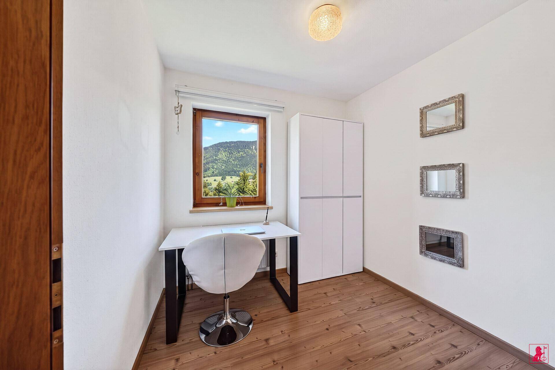 Kleines Arbeitszimmer mit Schreibtisch, Stuhl und Fenster mit Bergblick.