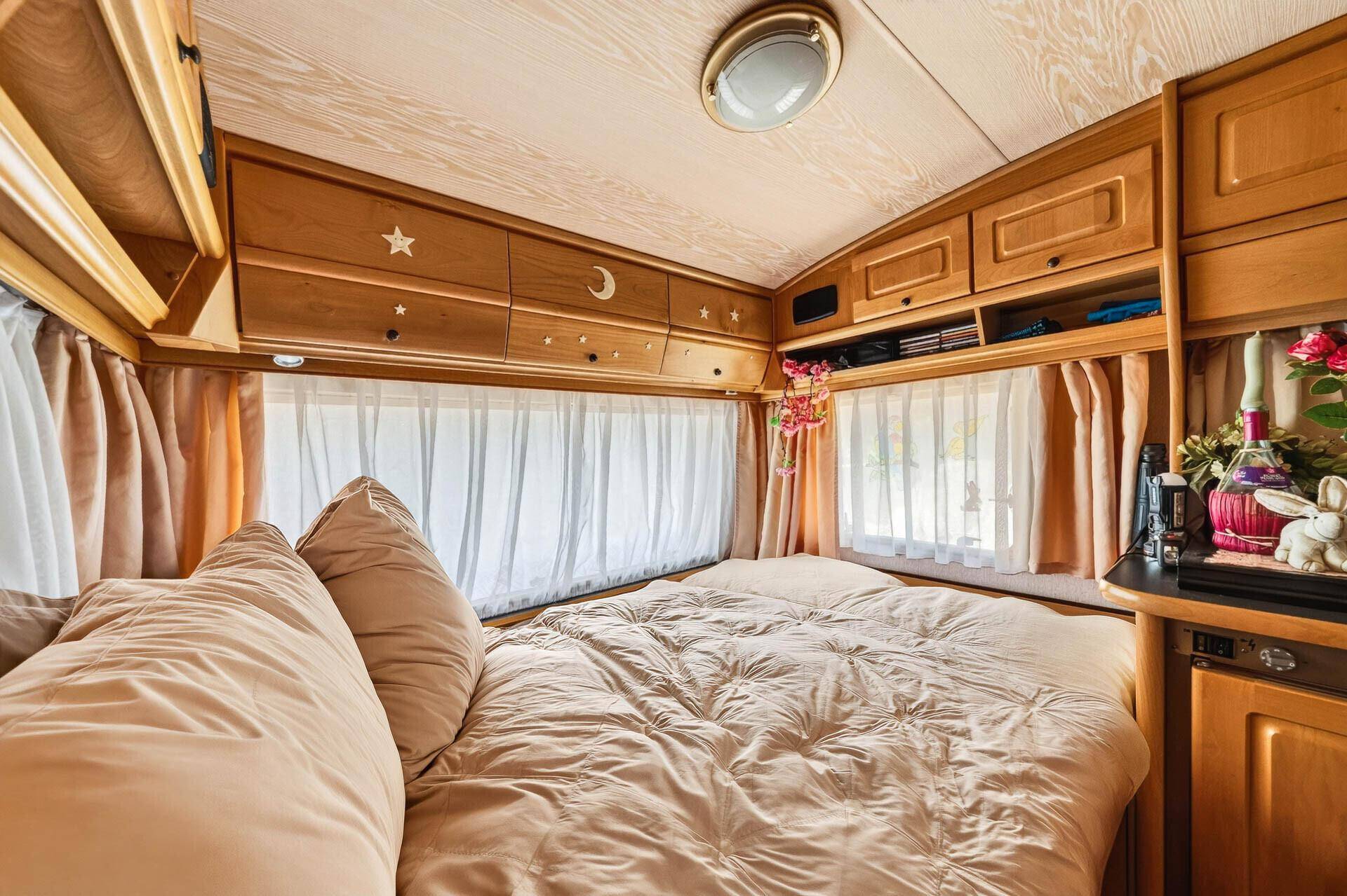 Helles Schlafzimmer mit Doppelbett, vielen Fenstern und Holzverkleidung im Wohnwagen.