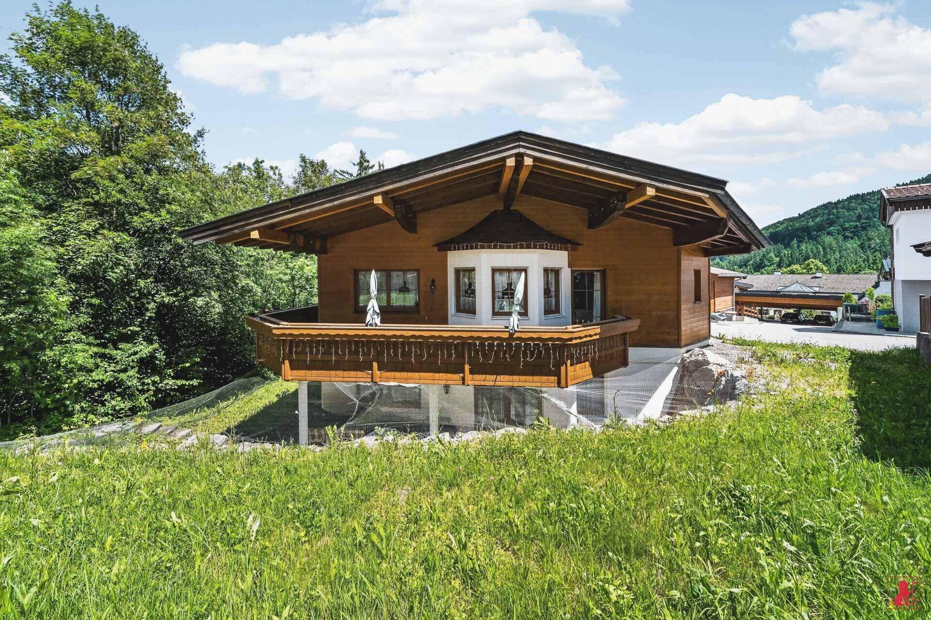 Traditionelles Holzhaus mit großem Balkon, umgeben von einer idyllischen grünen Landschaft.