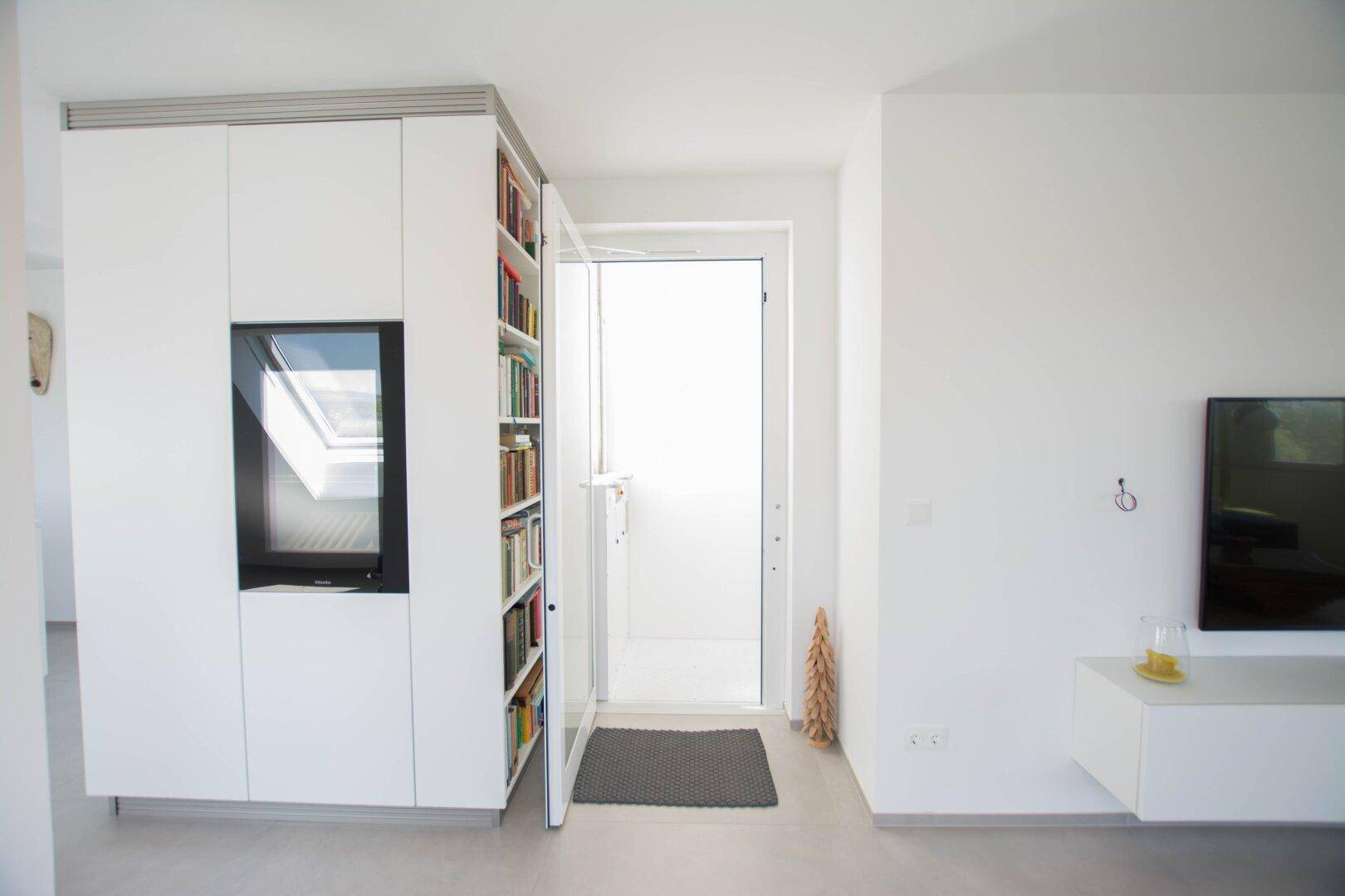 Eingangsbereich mit modernen Einbauschränken, Bücherregal und Zugang nach draußen.