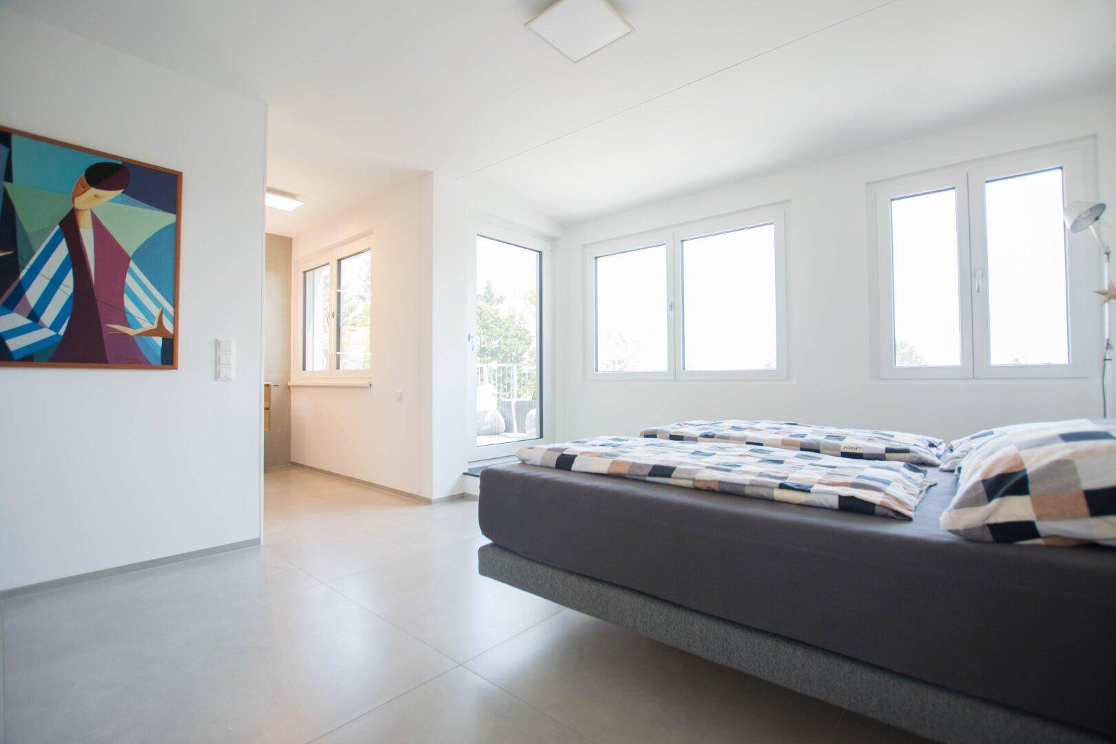 Helles Schlafzimmer mit modernem Bett, Fliesenboden und Zugang zu einem Balkon.