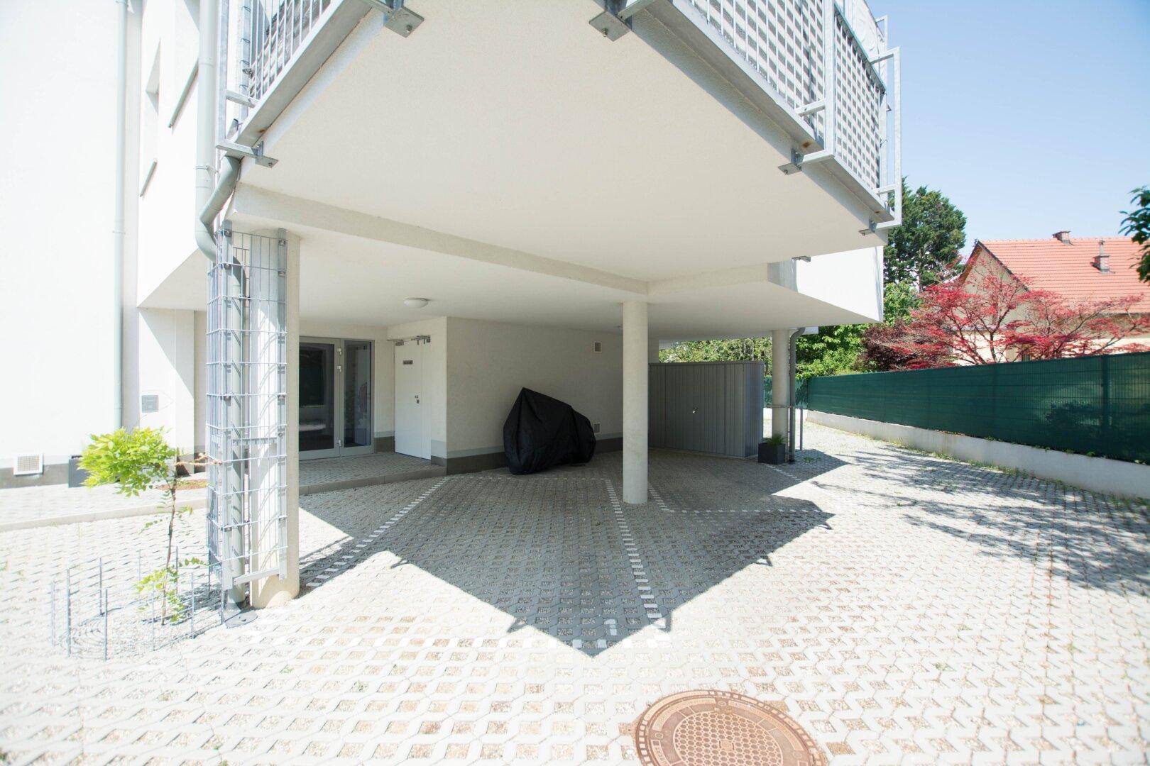 Überdachter Parkplatz unter dem Gebäude mit gepflasterter Zufahrt.