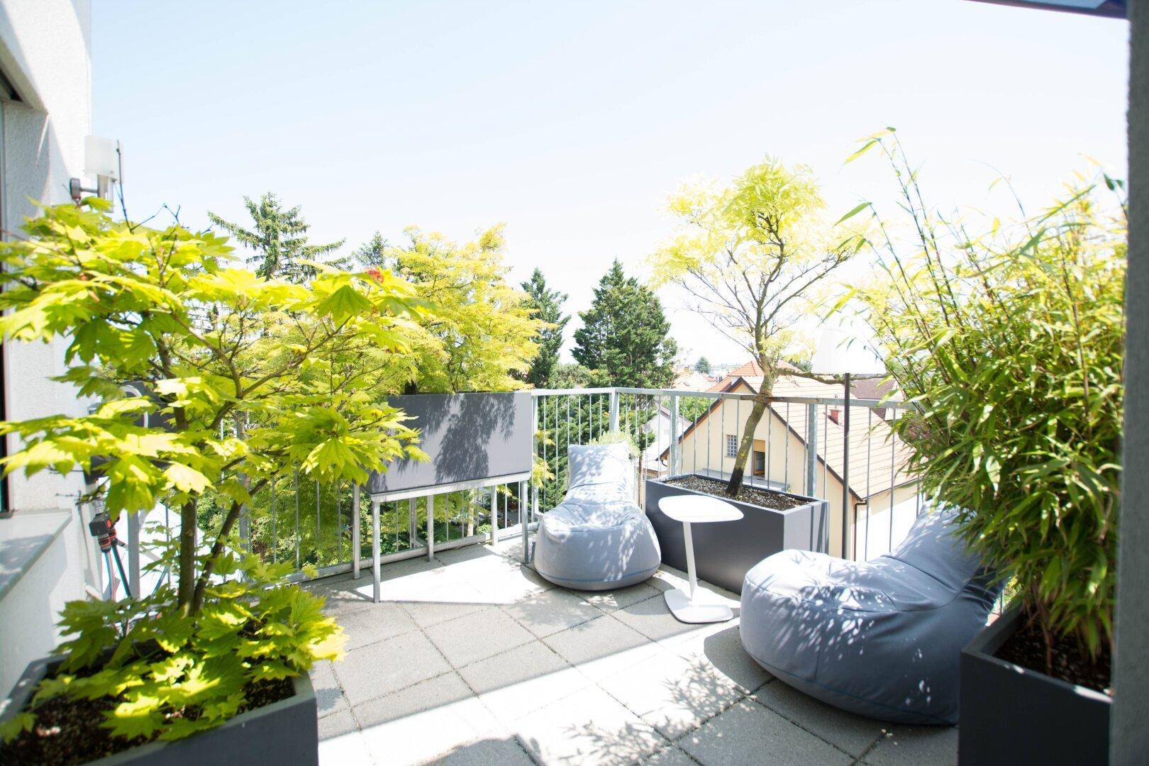 Sonniger Balkon mit bequemen Sitzsäcken, vielen Pflanzen und Blick über die Dächer.
