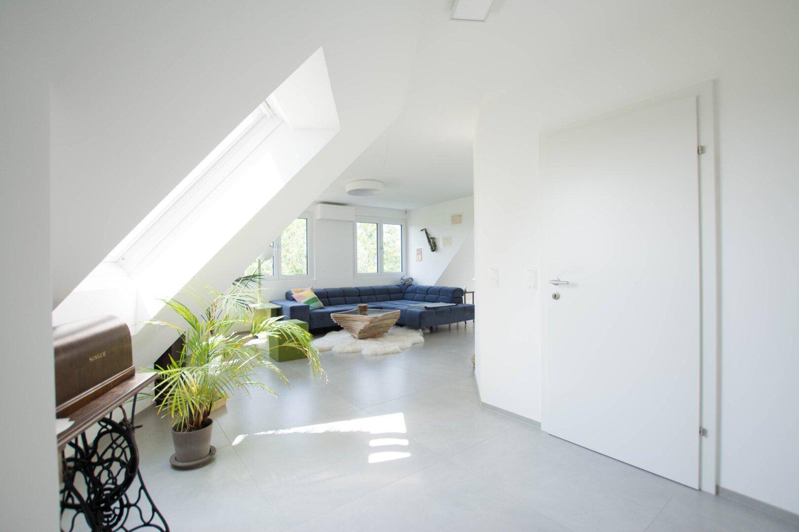 Geräumiger Wohnbereich mit blauer Couch, Dachschrägen und einem großen Dachfenster.