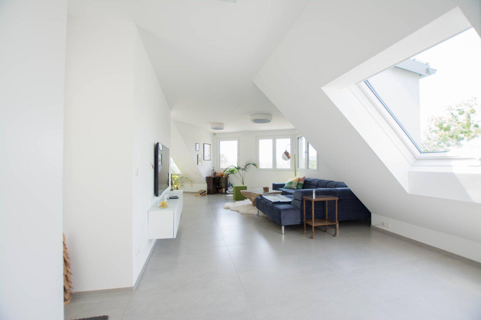 Heller Wohnbereich mit Dachschrägen, großem Dachfenster und moderner Einrichtung.