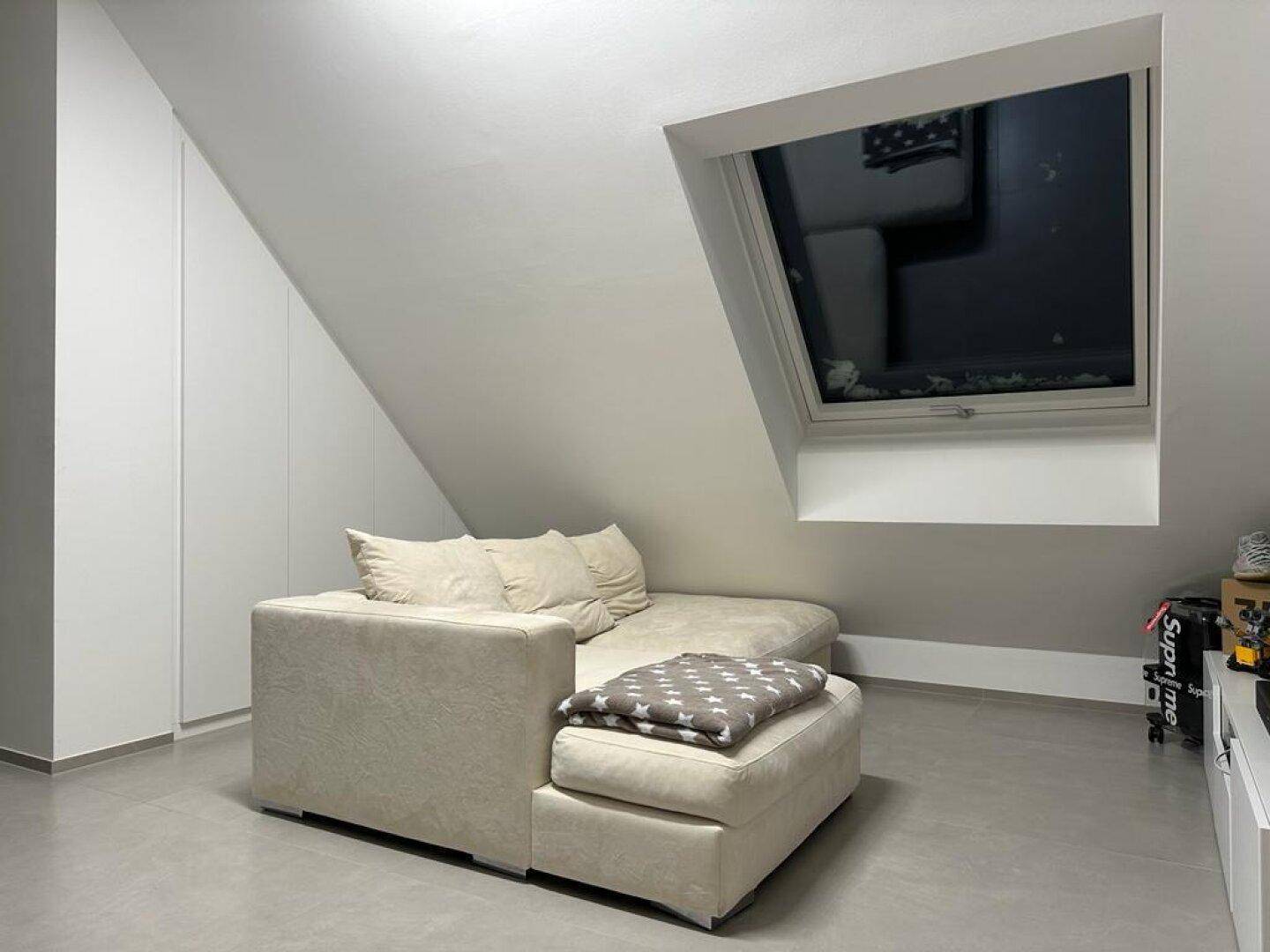Gemütlicher Wohnbereich mit Dachschrägen, Dachfenster und beigem Ecksofa.