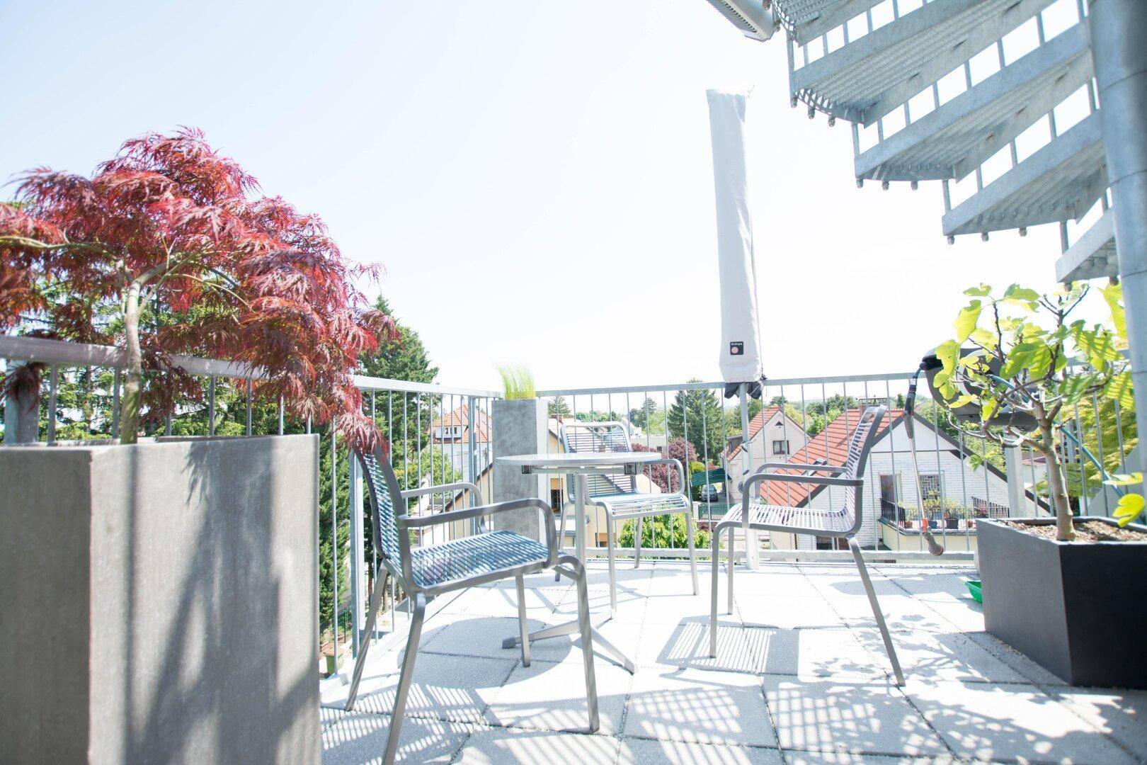 Sonniger Balkon mit Sitzgelegenheiten, Pflanzen und einer Wendeltreppe mit Blick auf die Umgebung.