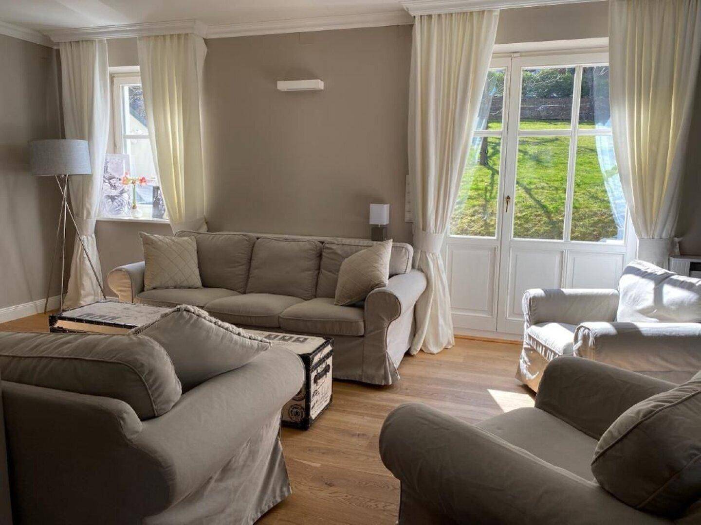Helles Wohnzimmer mit bequemen Sofas, Holzboden und Zugang zum grünen Garten.