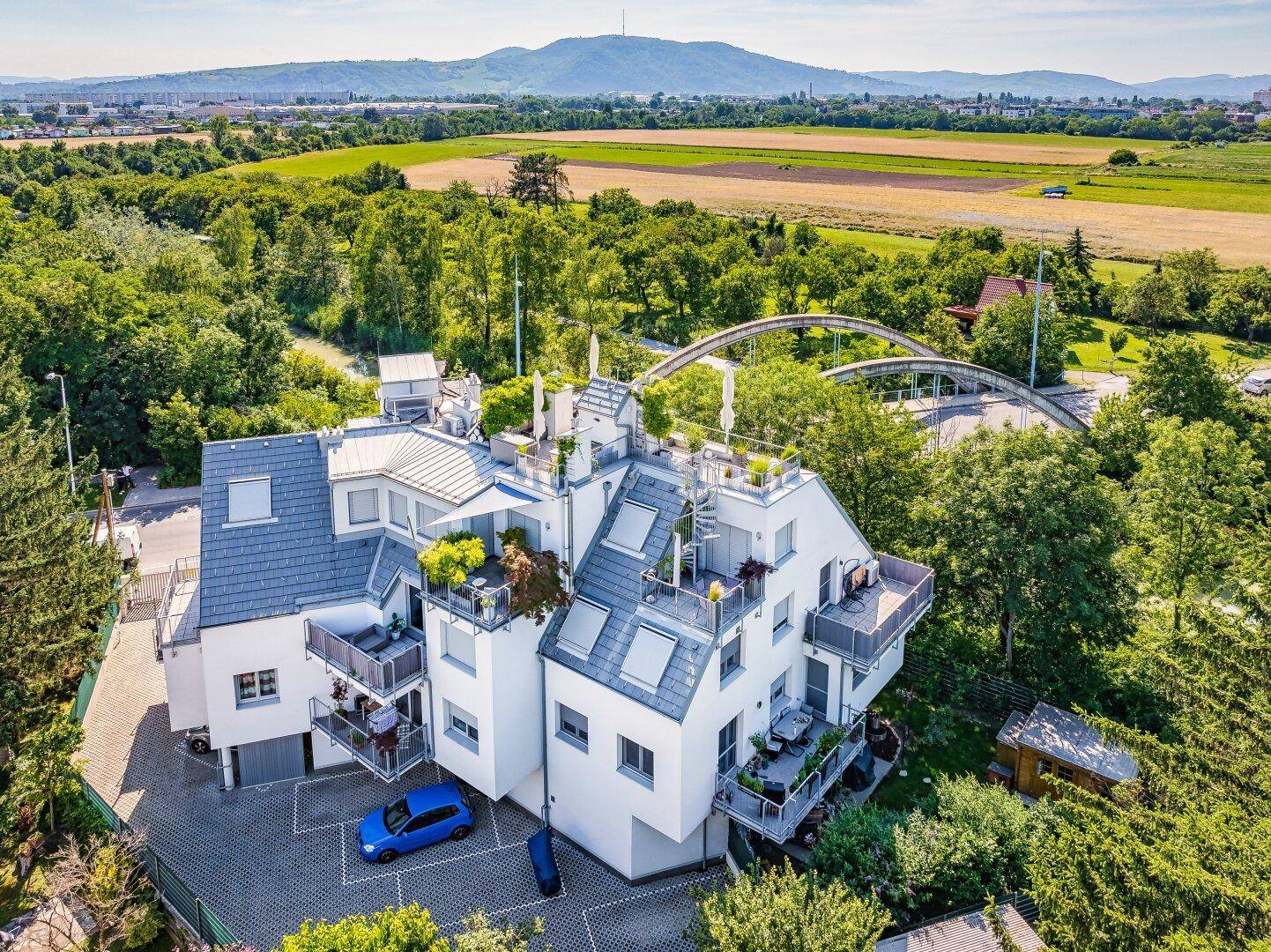 Moderne Wohnanlage in grüner Umgebung mit mehreren Balkonen, Terrassen und Blick auf die Landschaft und Berge.