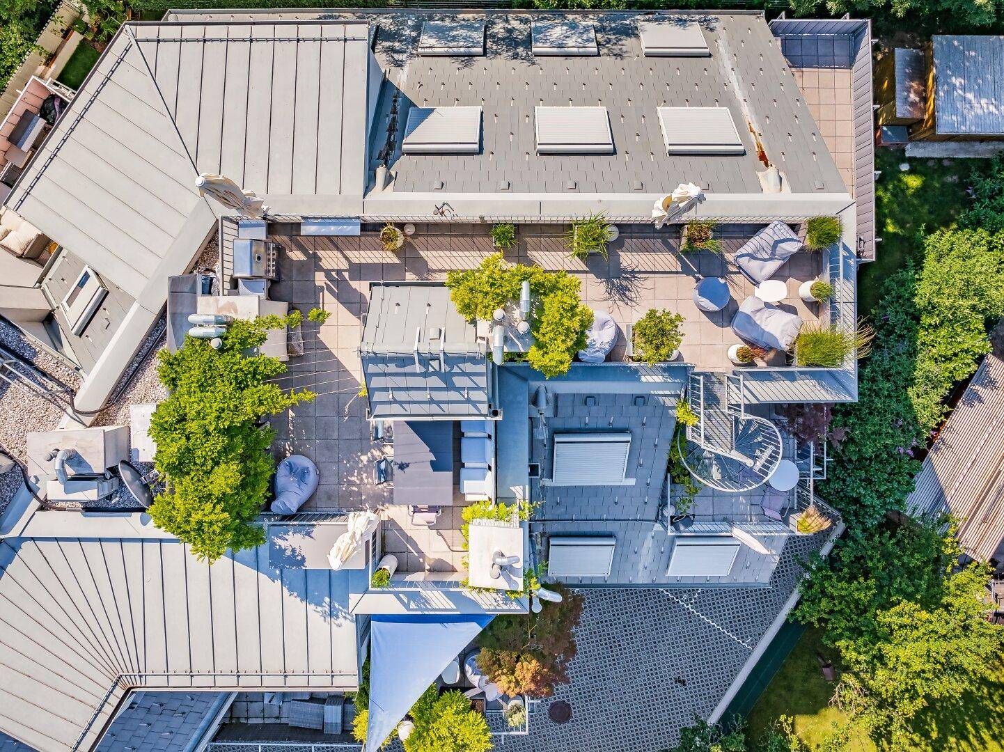 Draufsicht auf die weitläufigen Dachterrassen mit modernen Gartenmöbeln und Sonnenschirmen.