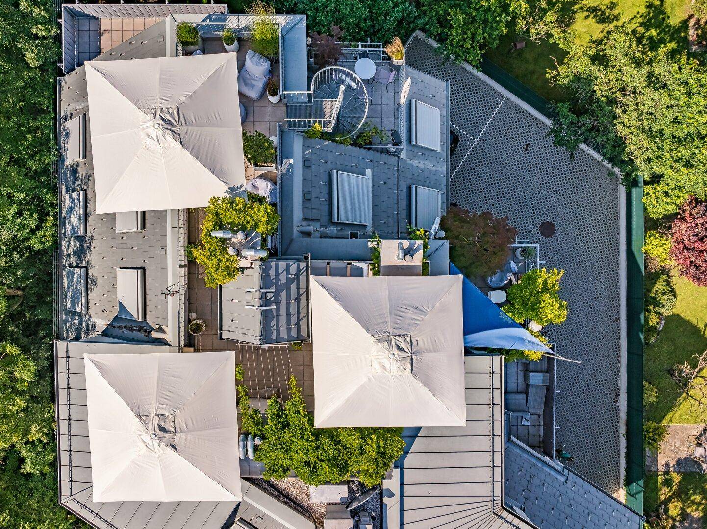 Ansicht von oben auf die Dachterrassen mit großen Sonnenschirmen und verschiedenen Sitzbereichen.