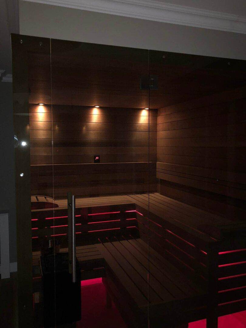 Moderne Sauna mit Holzverkleidung, Bänken und stimmungsvoller roter Beleuchtung.