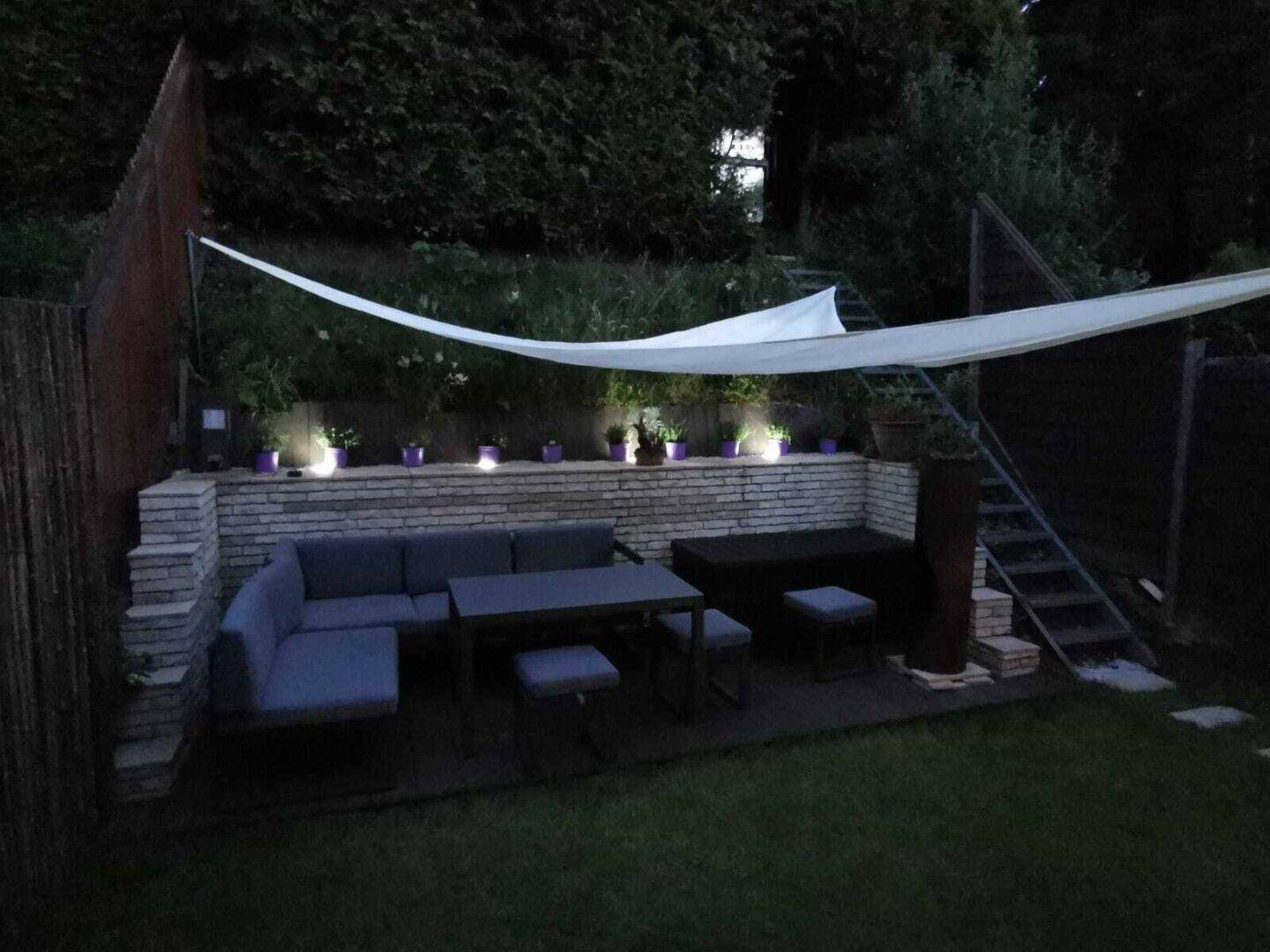 Beleuchteter Gartenbereich bei Nacht mit gemütlicher Sitzecke und stimmungsvoller Atmosphäre.