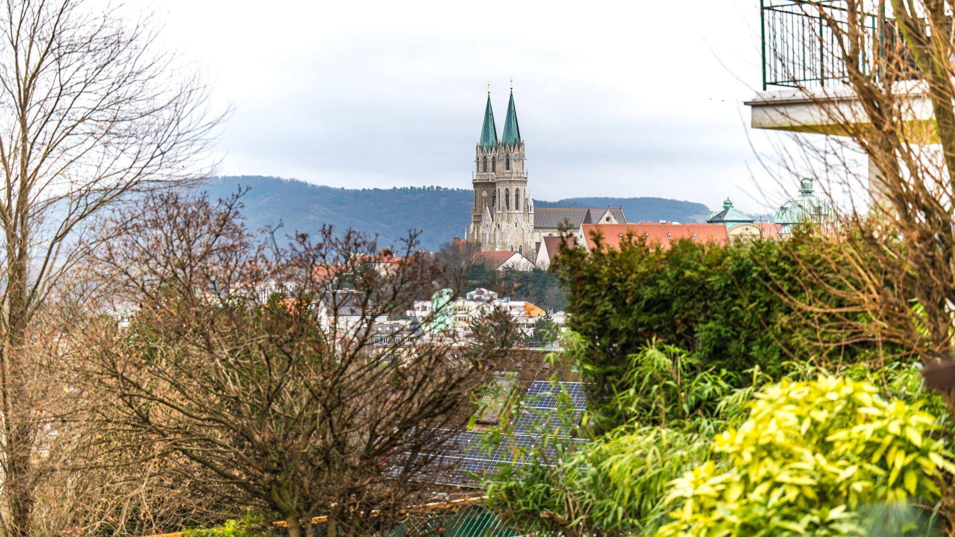 Panoramablick auf eine historische Kirche und die Stadt, umgeben von grünen Bäumen und Hügeln.