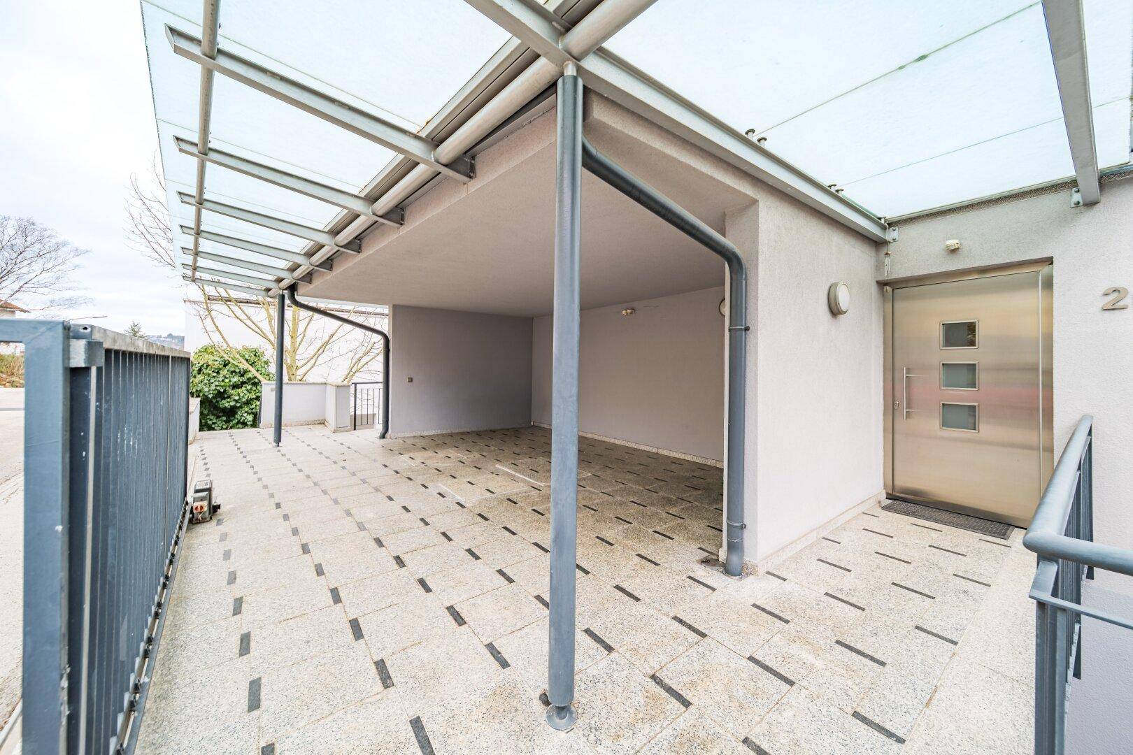 Überdachter Eingangsbereich mit Carport und moderner Haustür, gepflasterter Zufahrt.
