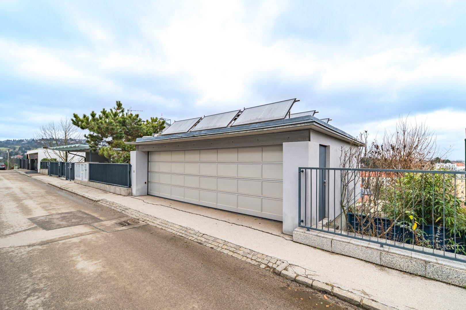 Moderne Garage mit Sektionaltor und Photovoltaikanlage auf dem Dach, an einer Wohnstraße gelegen.