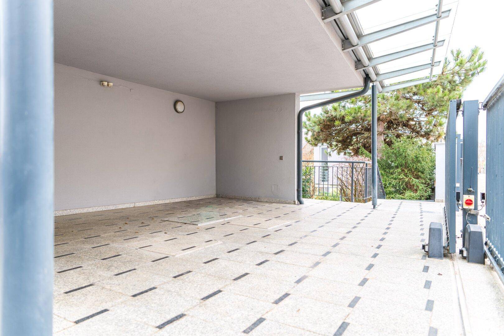 Geräumiger Carport mit Fliesenboden und Glasdach, bietet geschützten Stellplatz.