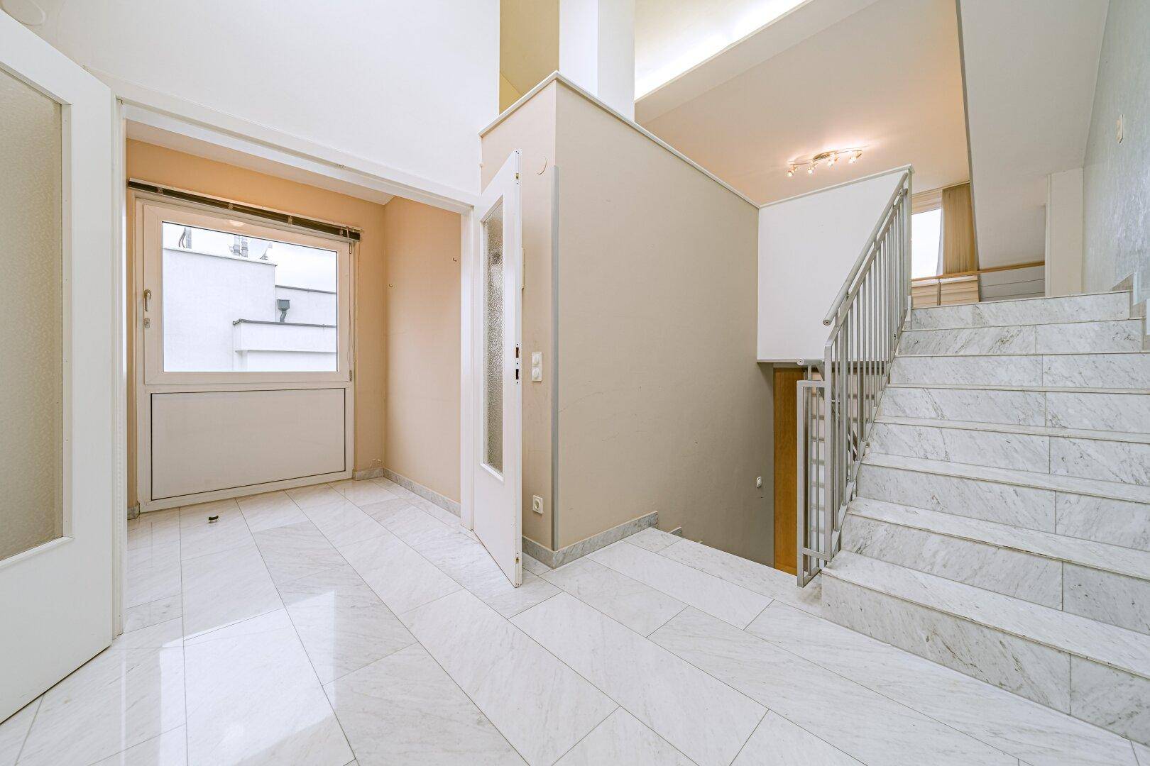 Heller Eingangsbereich mit Marmorfliesen, Treppe und Zugang zu weiteren Räumen.