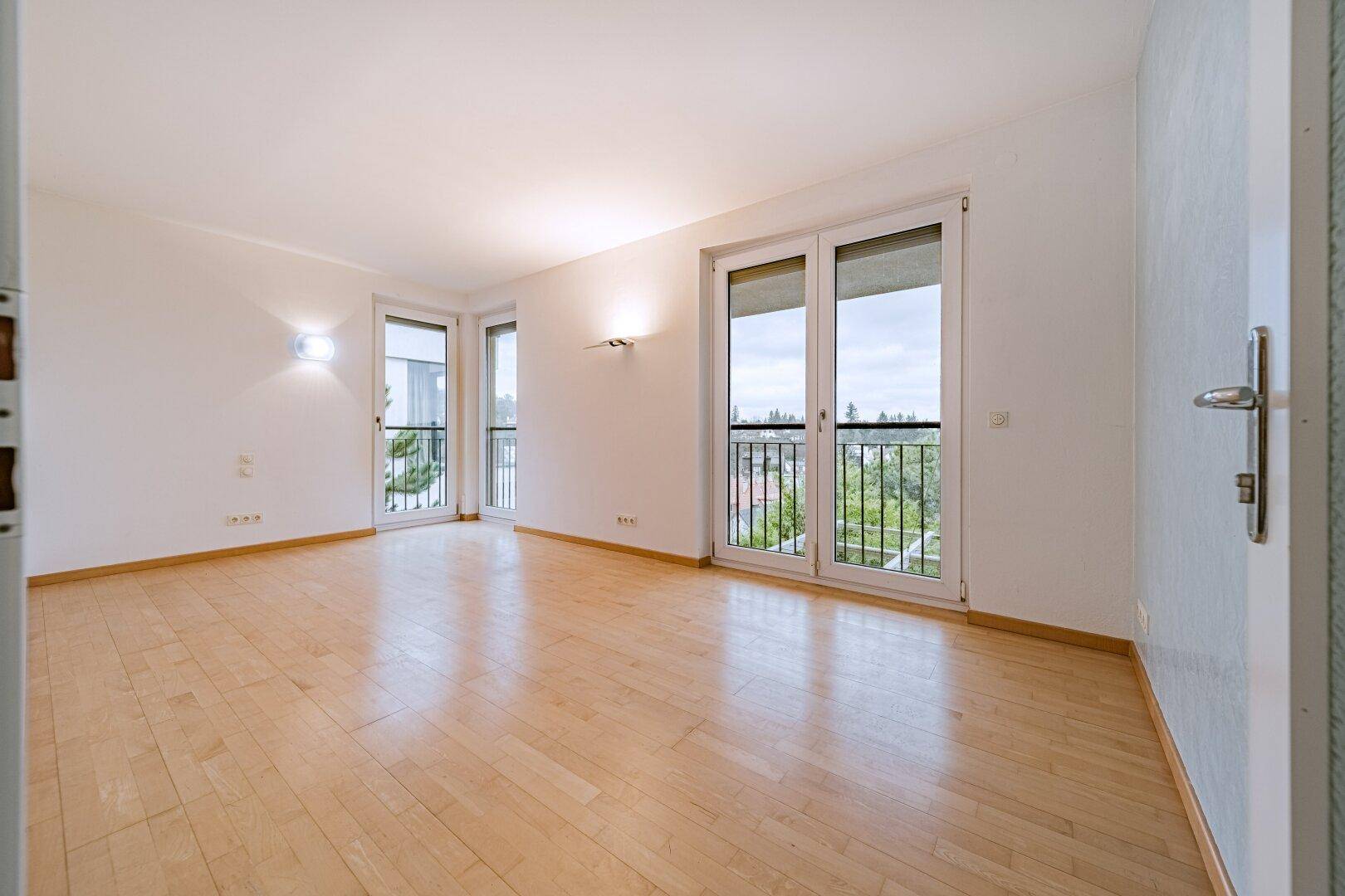 Heller Raum mit Holzboden und zwei französischen Balkonen, bietet viel Tageslicht.