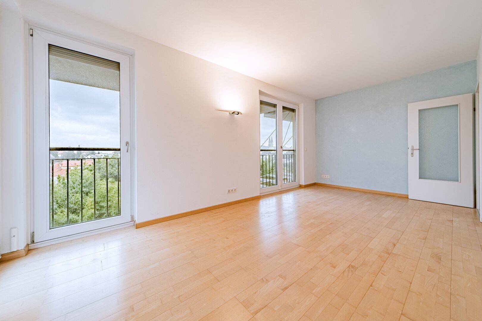 Geräumiger Raum mit Holzboden, hellblauer Akzentwand und französischen Balkonen.