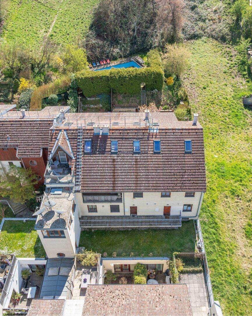 Luftaufnahme eines Wohngebäudes mit Dachfenstern, Terrassen und einem Pool im Hintergrund.