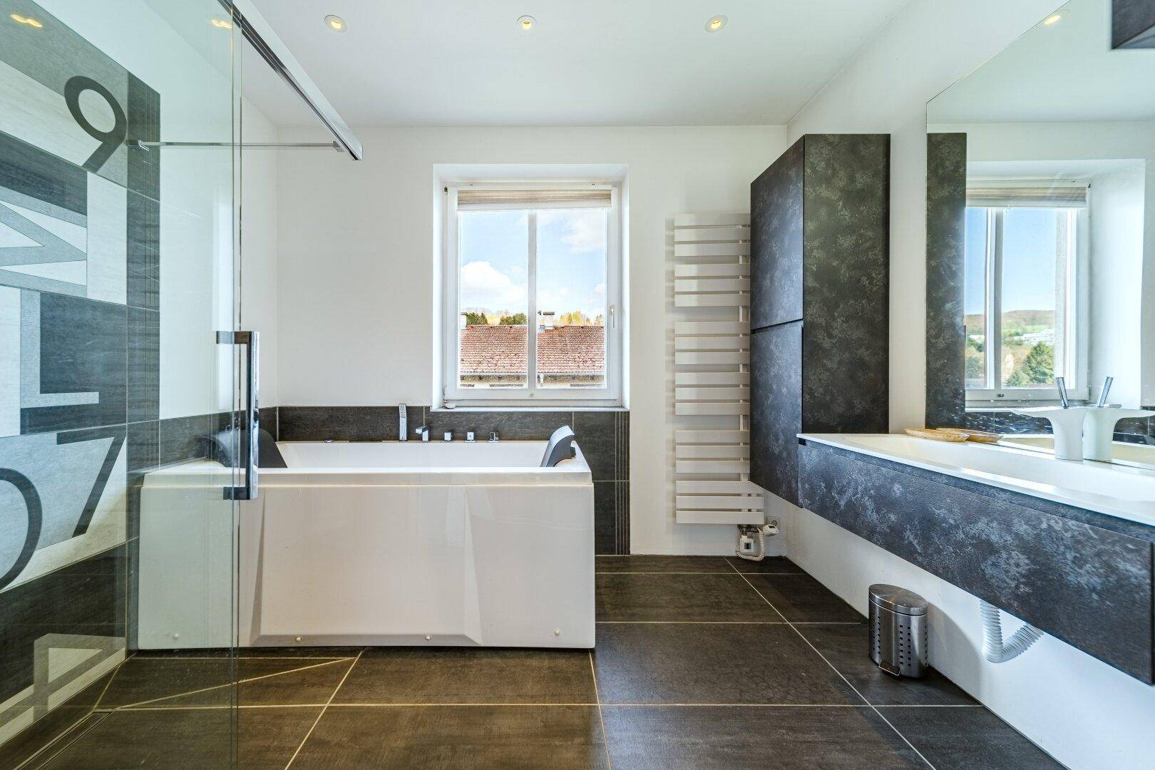 Modernes Badezimmer mit Badewanne, Dusche und dunklen Fliesen.