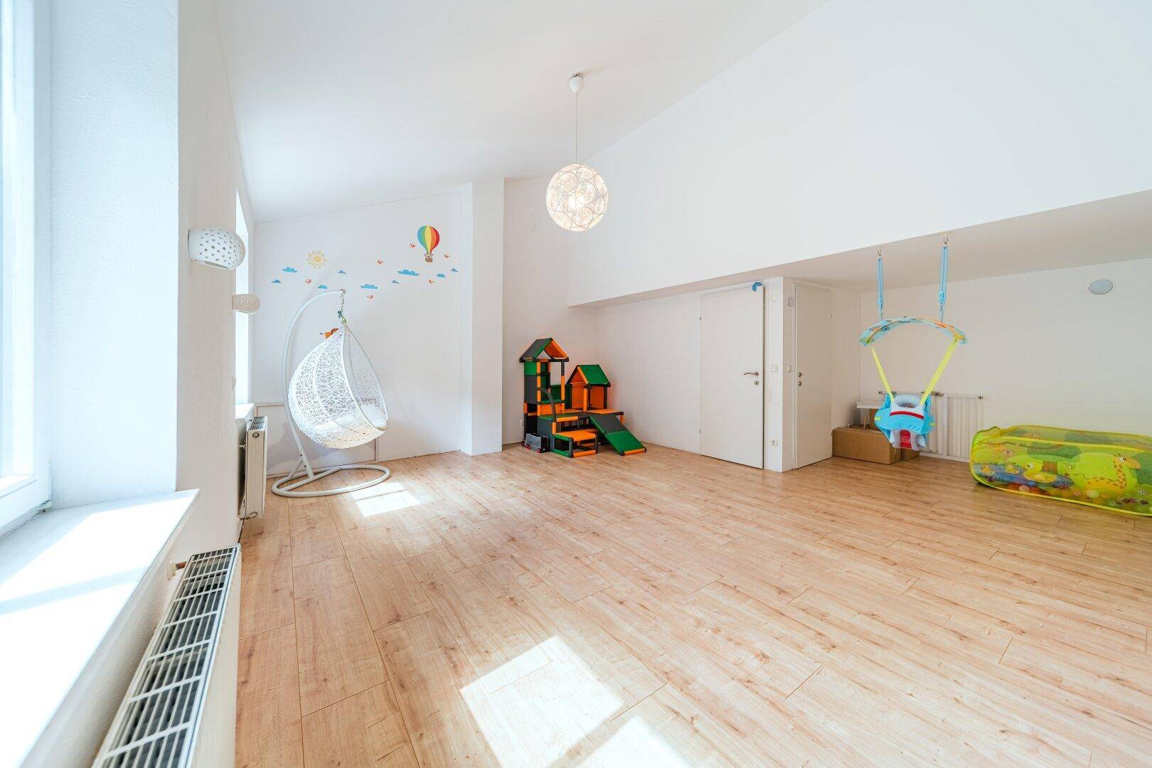 Helles Kinderzimmer oder Spielzimmer mit Holzboden, Spielgeräten und Schaukeln.