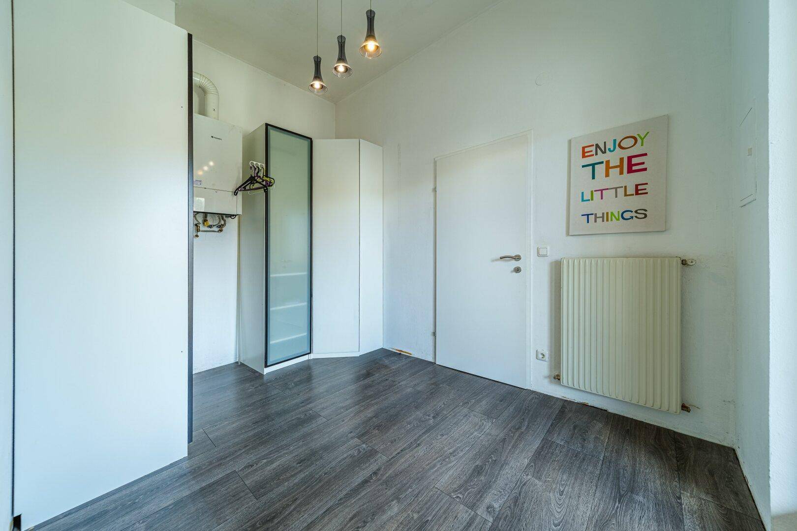 Flur oder Hauswirtschaftsraum mit Heizungsanlage, Schränken und dunklem Boden.
